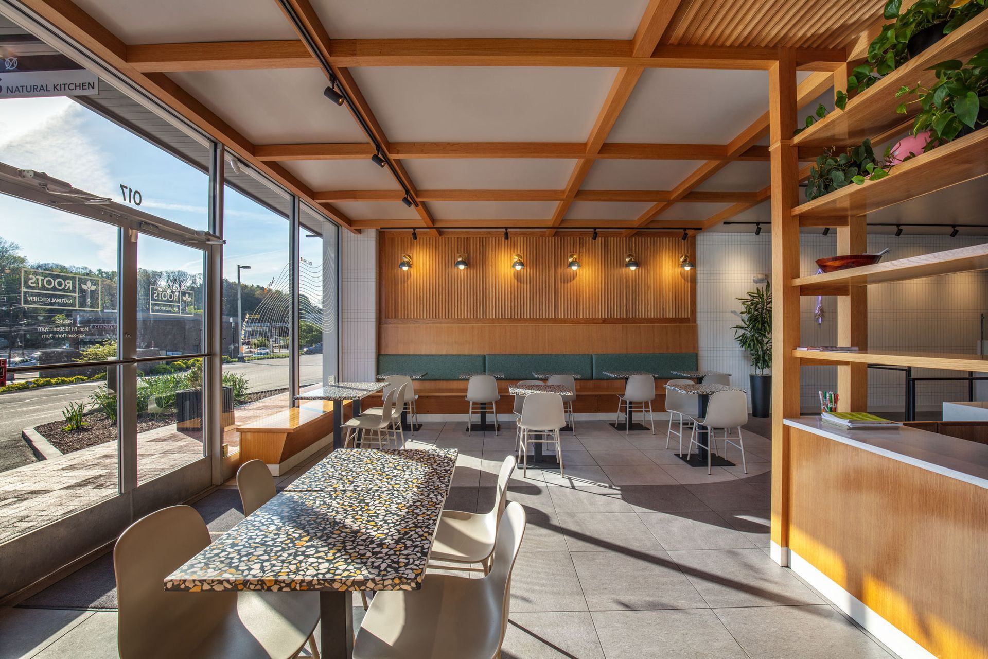 Roots Natural Kitchen's interior with wooden beams, large windows, and sunlight on tables and chairs.