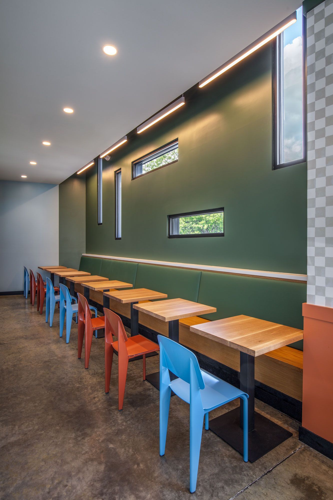 Long row of colorful chairs and wooden tables beside a green wall in Roots Natural Kitchen's interior