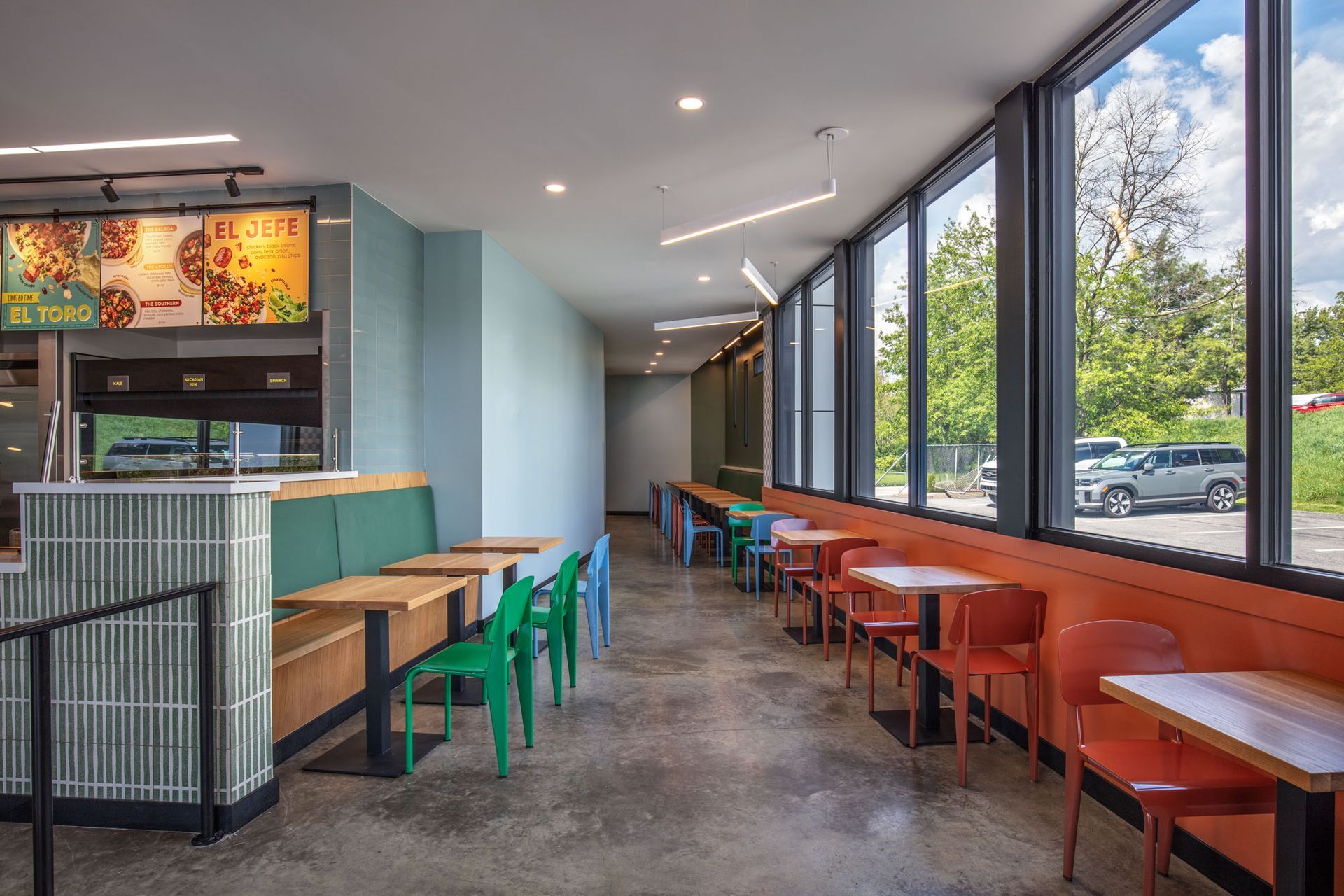Roots Natural Kitchen's interior with long tables, colorful chairs, and large windows along one side