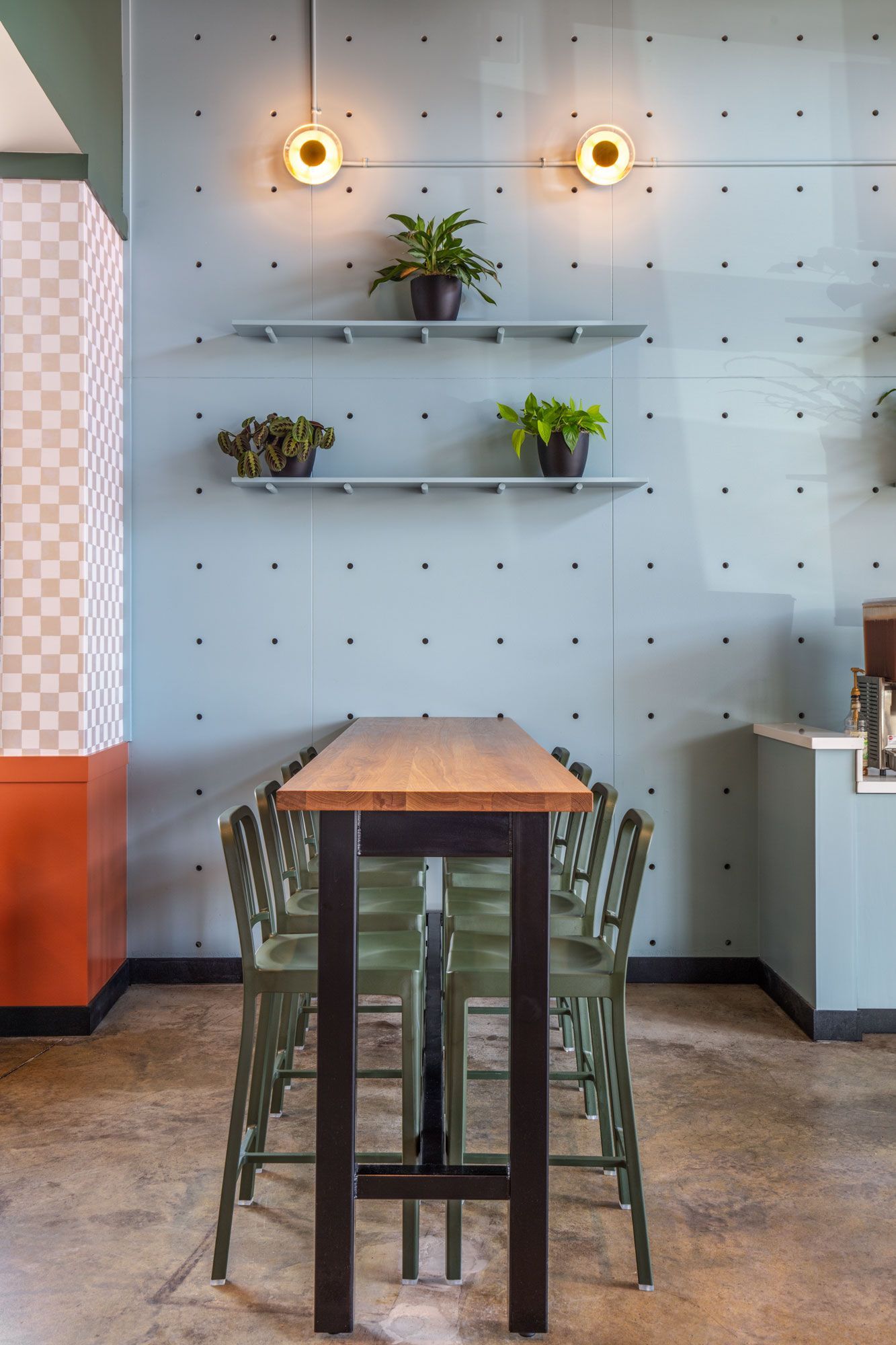 Roots Natural Kitchen's interior table and chairs against a light blue wall with shelves, plants, and warm pendant lights