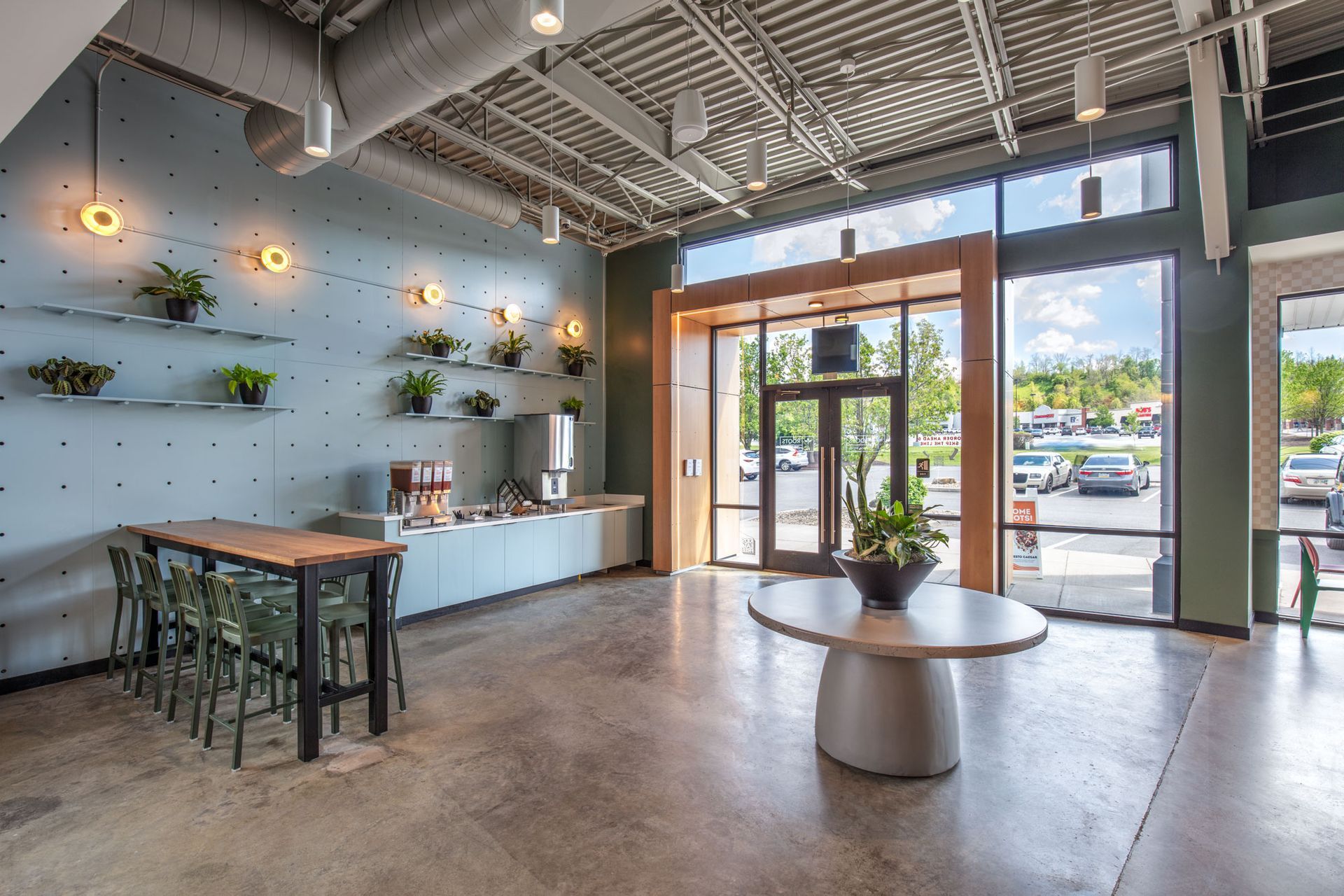 Roots Natural Kitchen's interior with communal table, wall shelves, pendant lights, and large front windows.