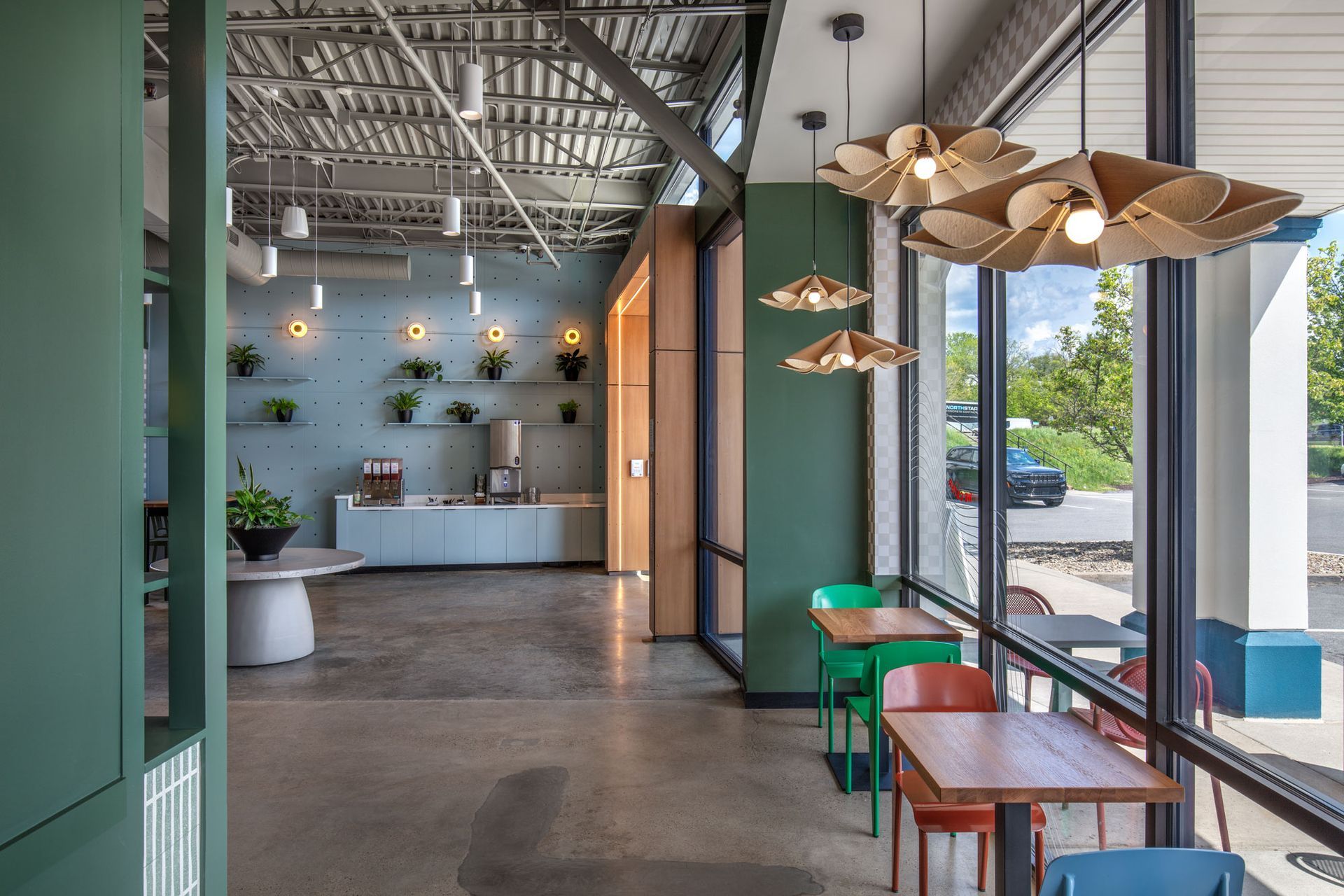 Roots Natural Kitchen's interior with teal walls, hanging lights, and tables by large windows overlooking a street