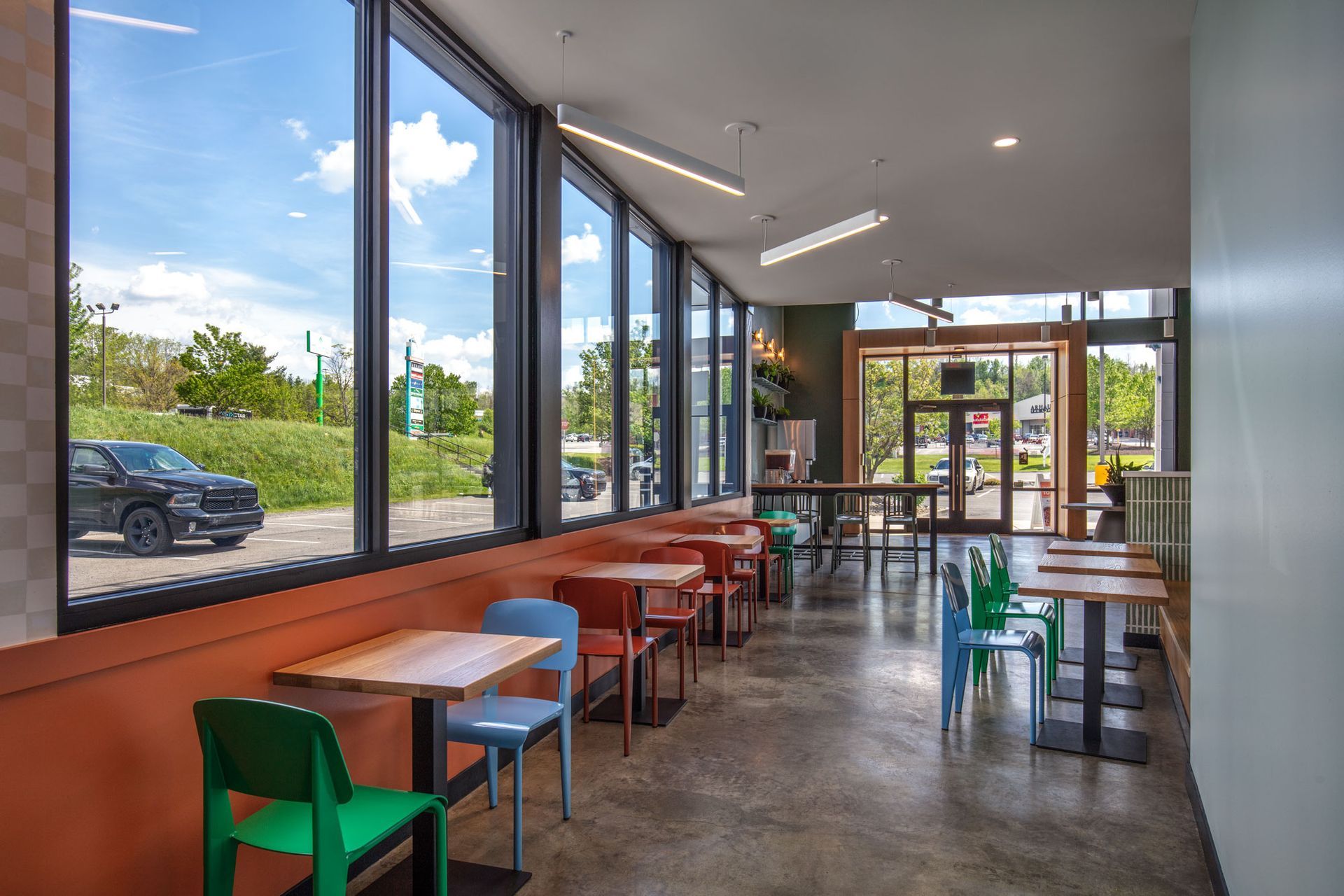Roots Natural Kitchen's interior with wooden tables, colorful chairs, and large windows overlooking parked cars outside