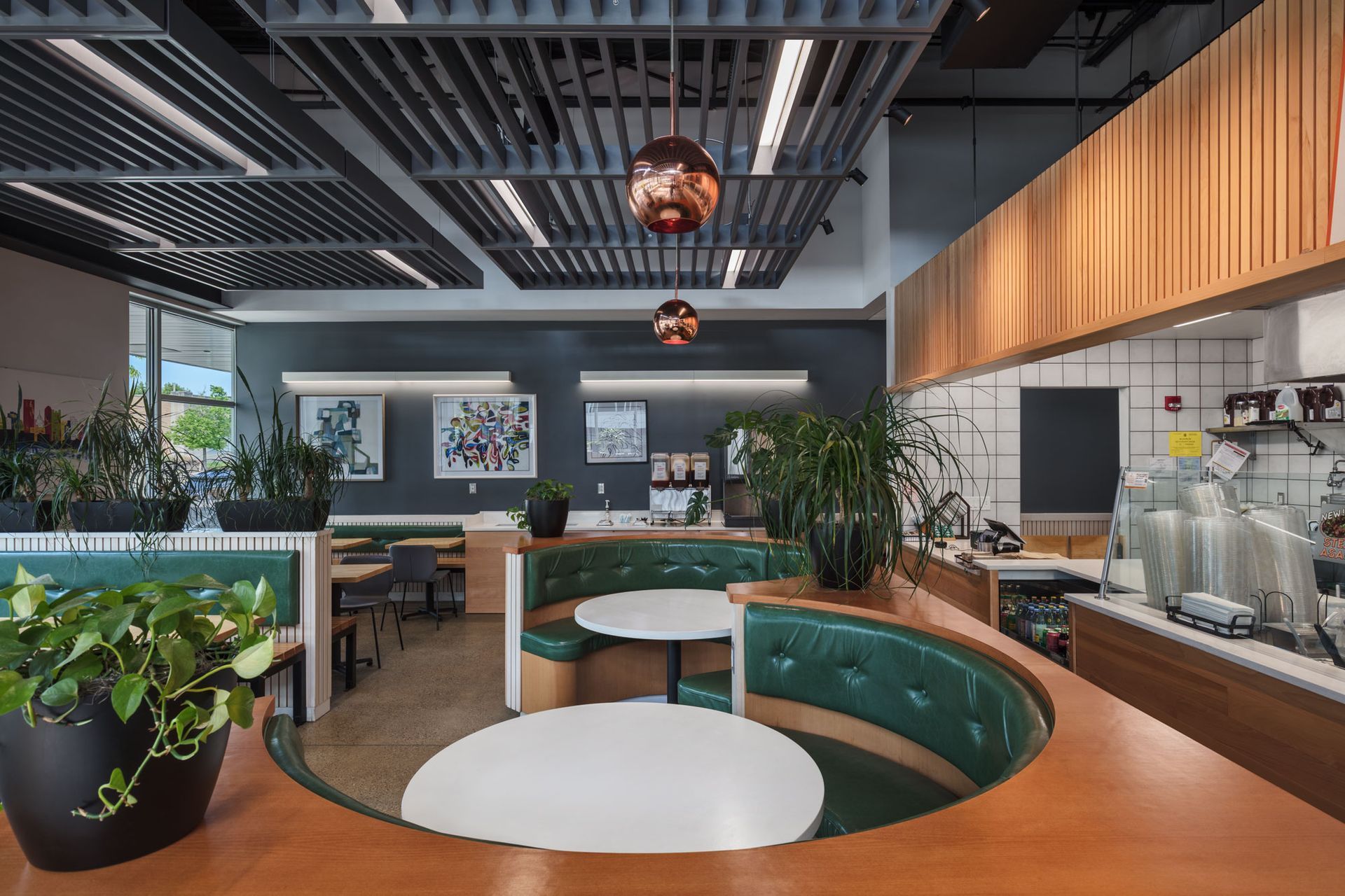 Roots Natural Kitchen's interior with wood accents, teal seating, plants, and pendant lights