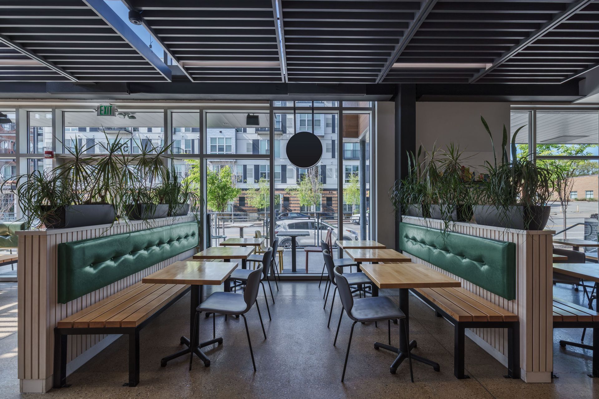 Roots Natural Kitchen's interior seating with green banquettes, wooden tables, and large windows overlooking a city street