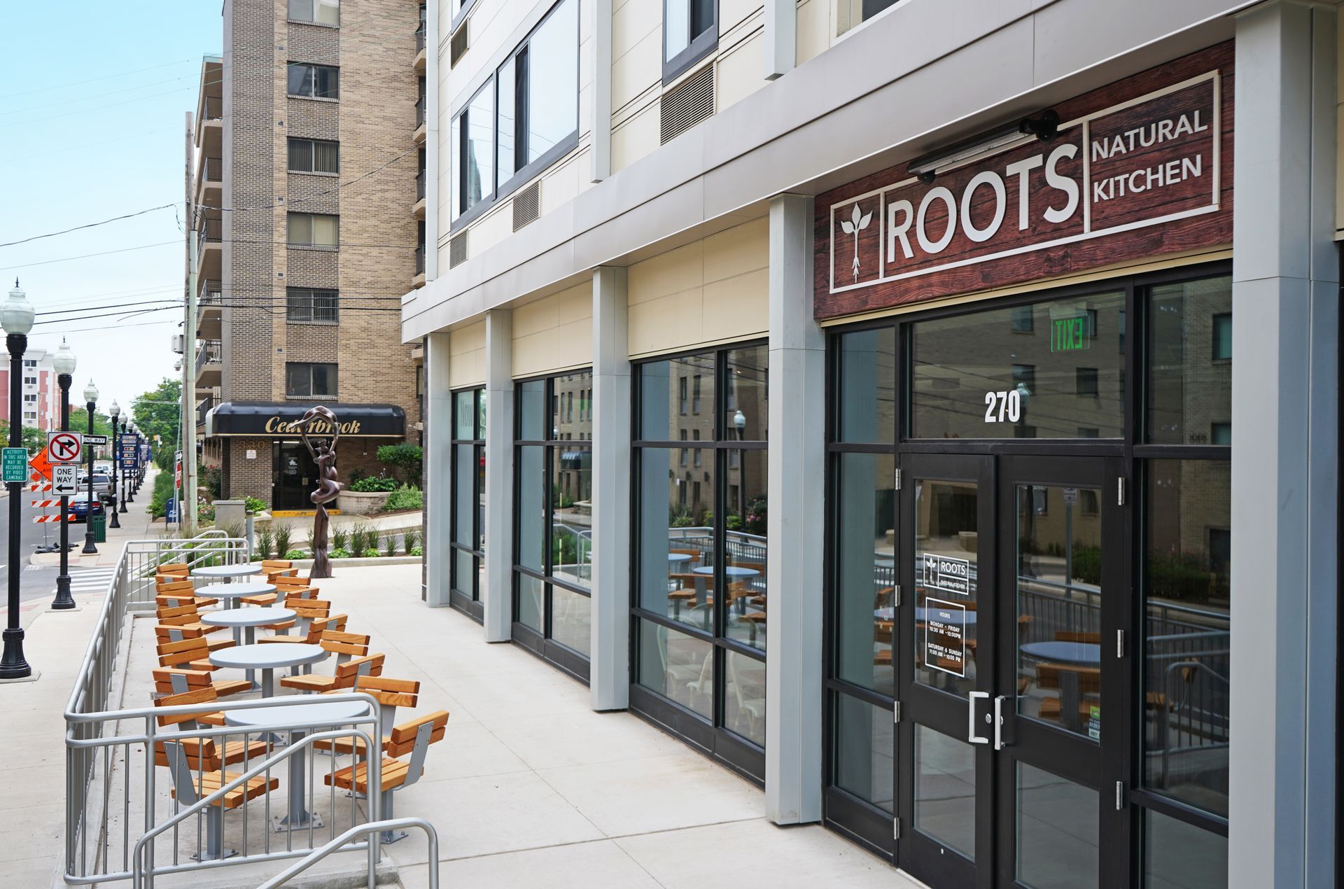 Roots Natural Kitchen's outdoor restaurant patio with orange chairs beside a storefront labeled “ROOTS” on a city sidewalk