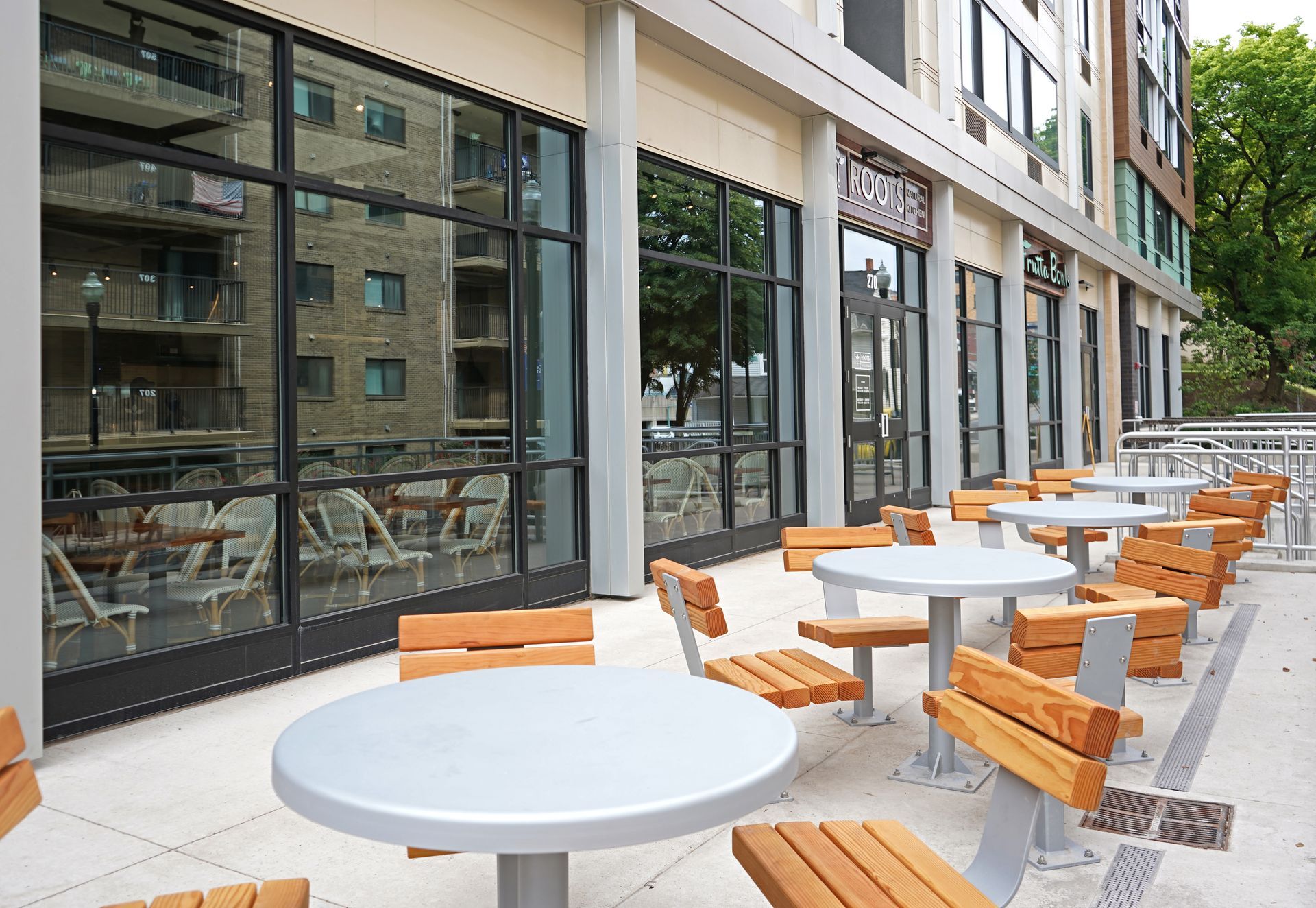 Roots Natural Kitchen's outdoor seating with white tables and orange benches beside large glass windows