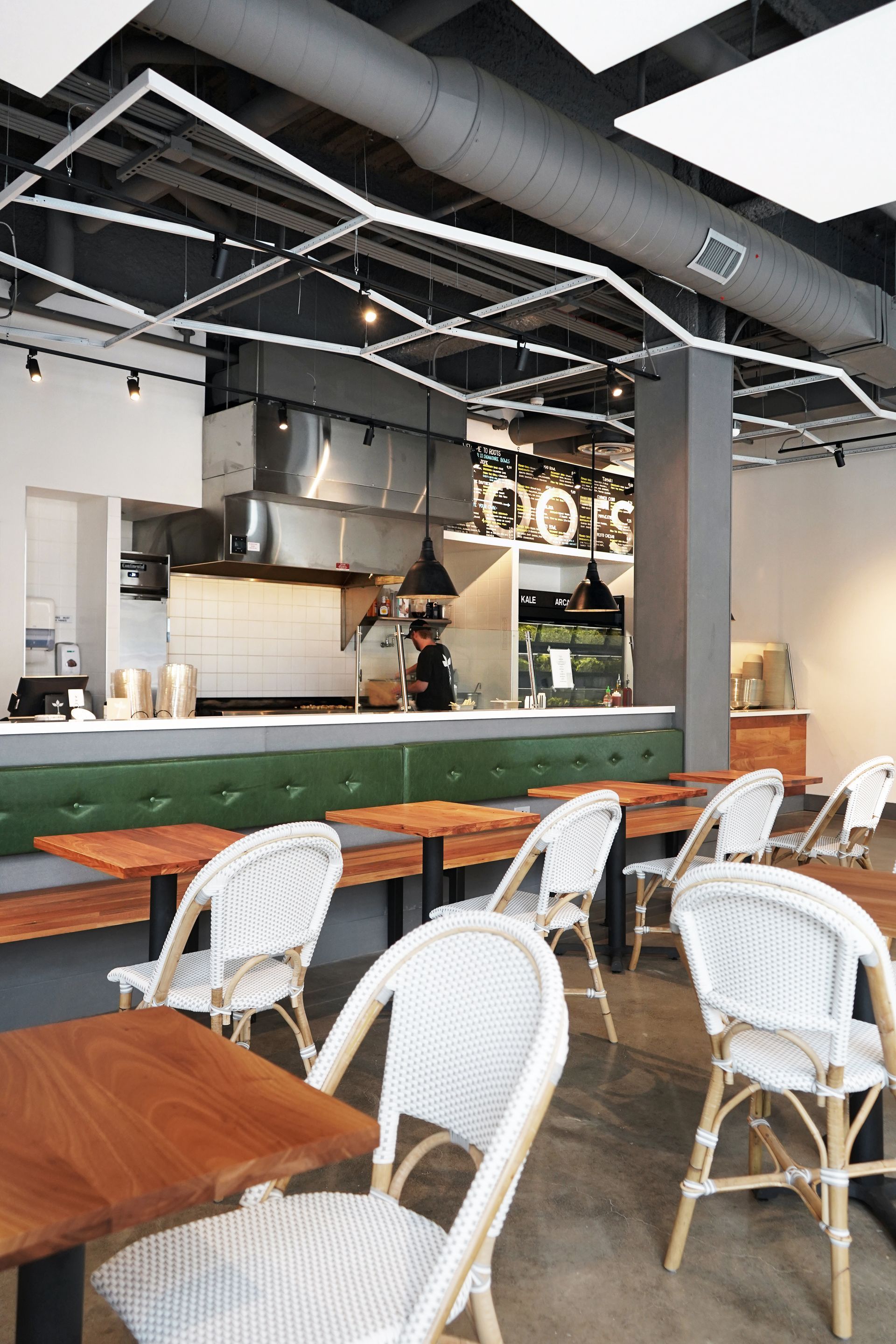 Roots Natural Kitchen's interior with white chairs, wooden tables, and a green partition near an open kitchen.