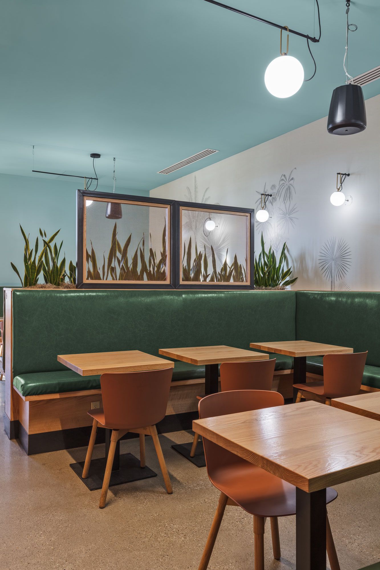 Roots Natural Kitchen's seating with wooden tables and chairs, green banquettes, and hanging pendant lights