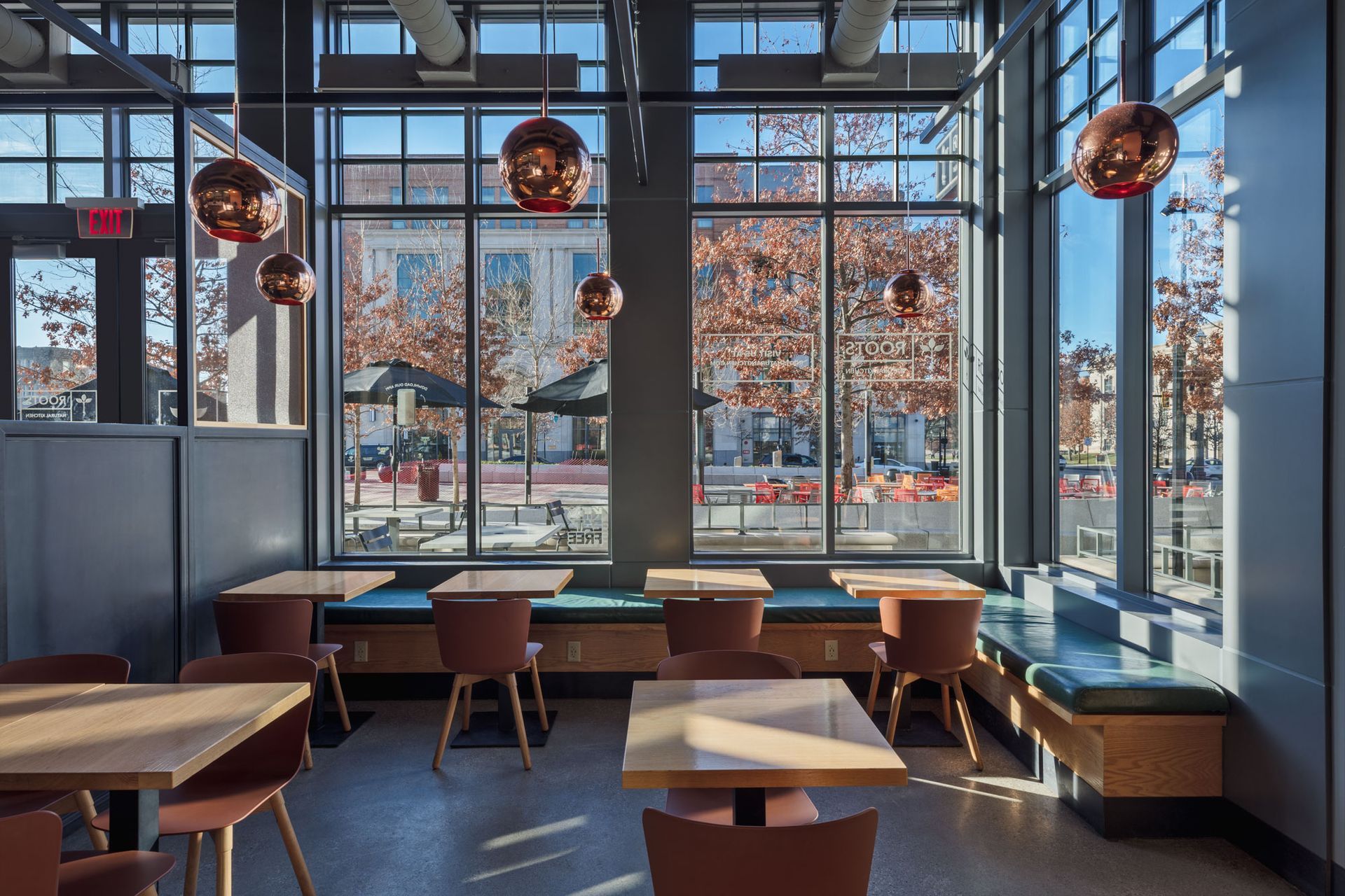Roots Natural Kitchen with large windows, wooden tables, stools, and hanging globe lights