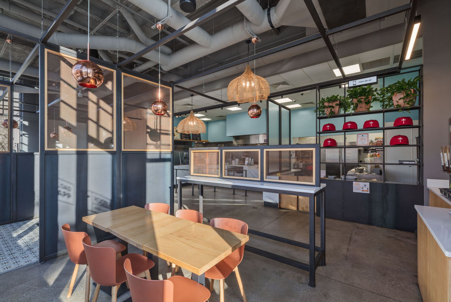 Roots Natural Kitchen's interior with wooden tables, orange chairs, hanging lights, and display shelves by large windows
