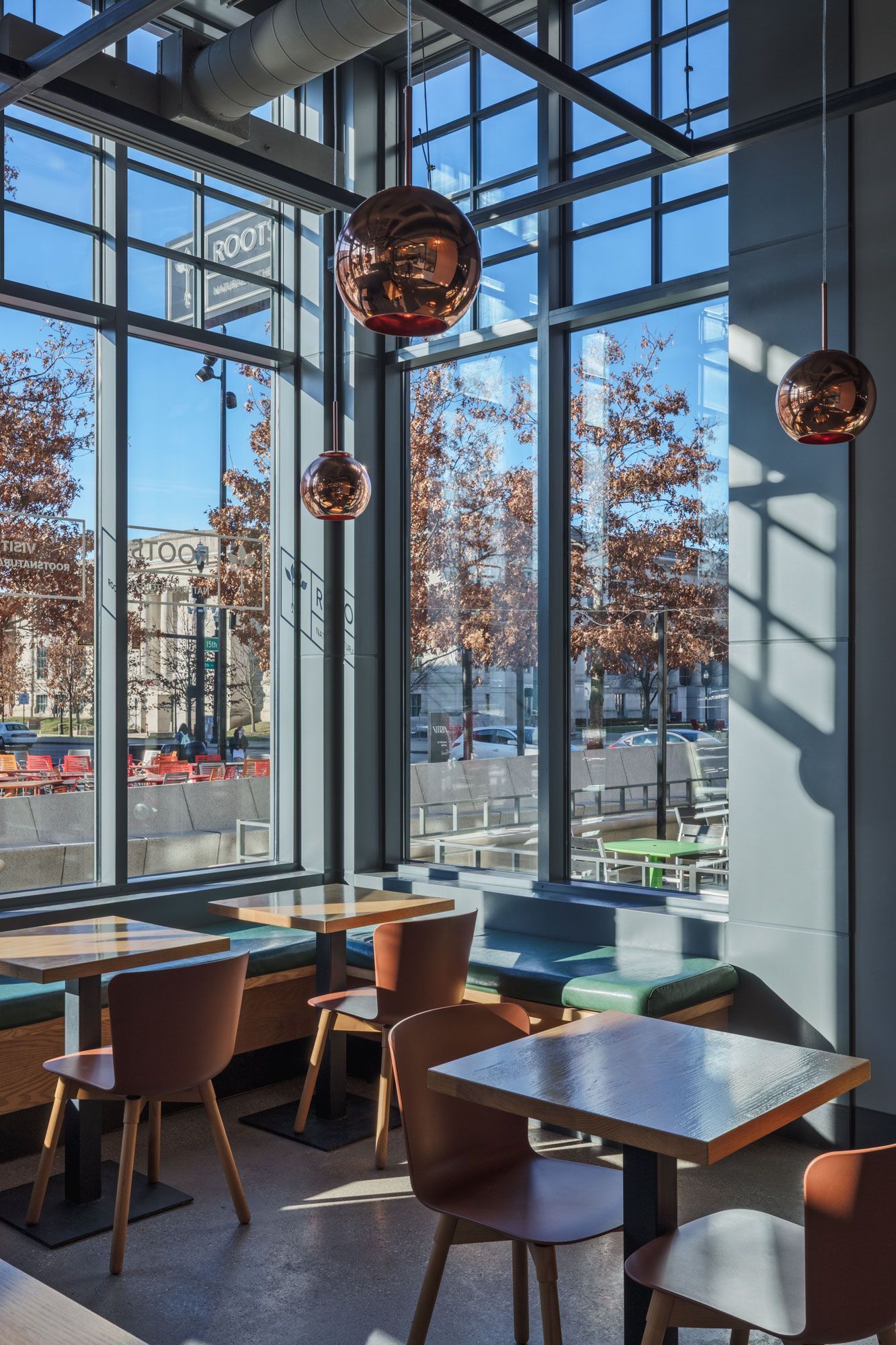 Roots Natural Kitchen with large windows, wooden tables, and copper pendant lights overlooking autumn trees