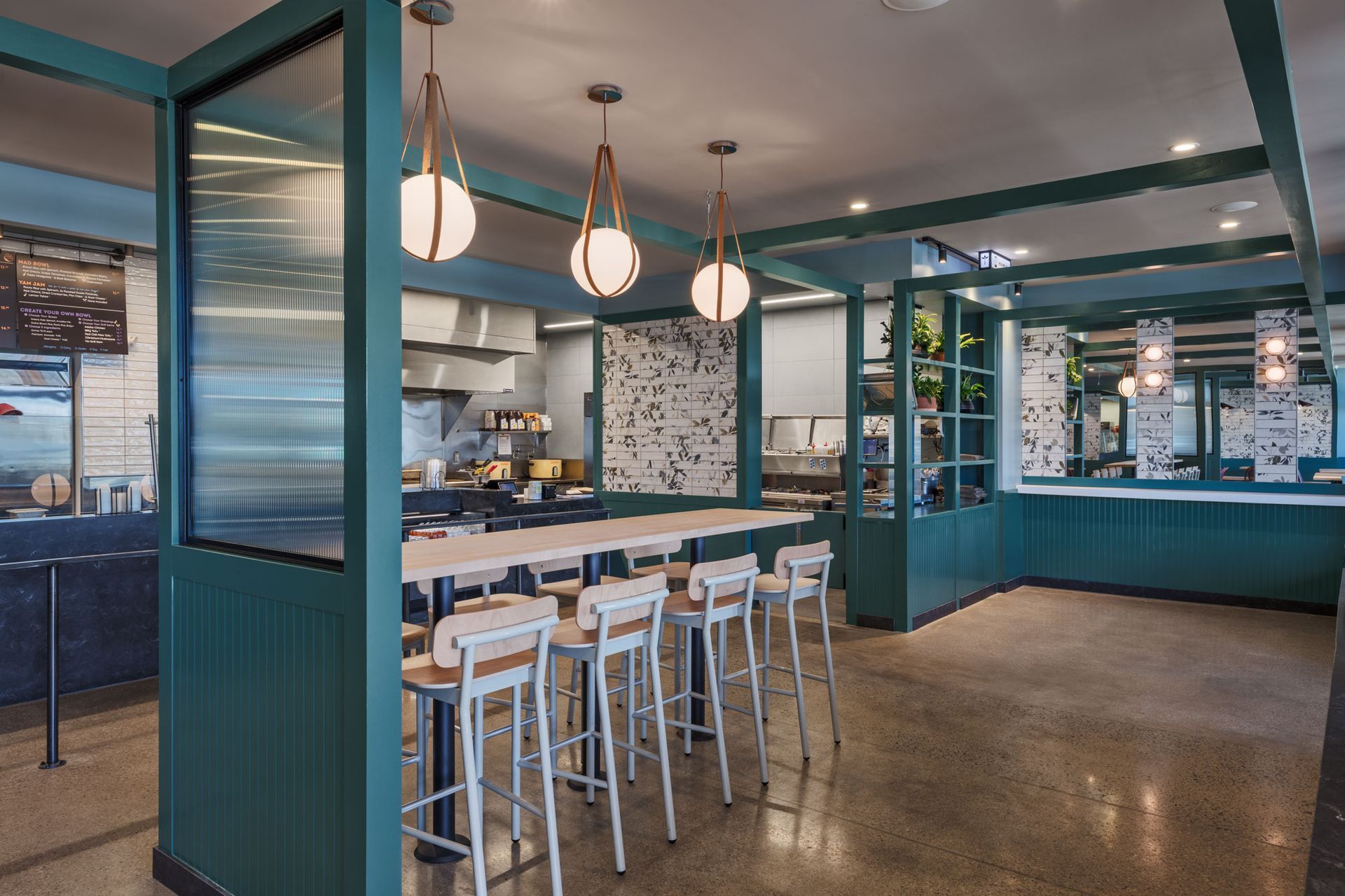 Roots Natural Kitchen's interior with a bar counter, stools, pendant lights, and large windows