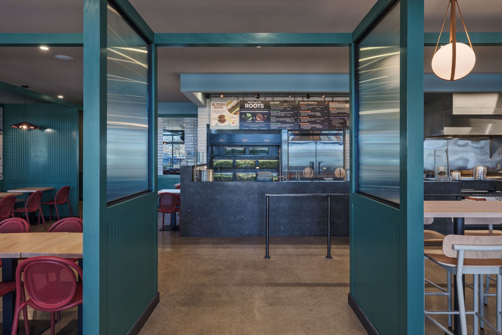 Roots Natural Kitchen's entryway facing a bar with shelves, stools, and warm pendant lighting