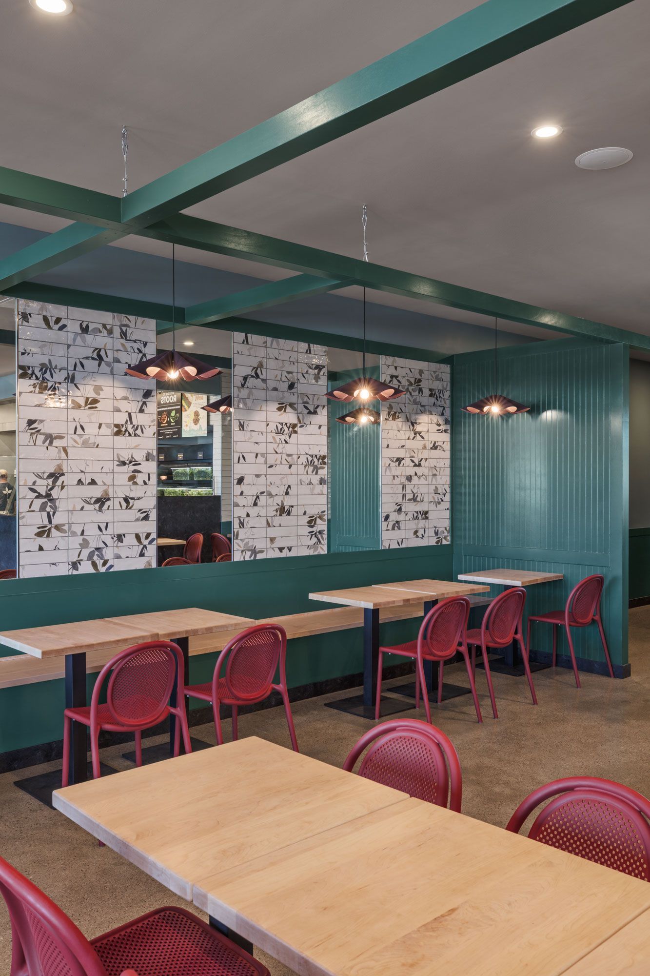 Roots Natural Kitchen with wooden tables, red chairs, teal beams, and wall-mounted lights.