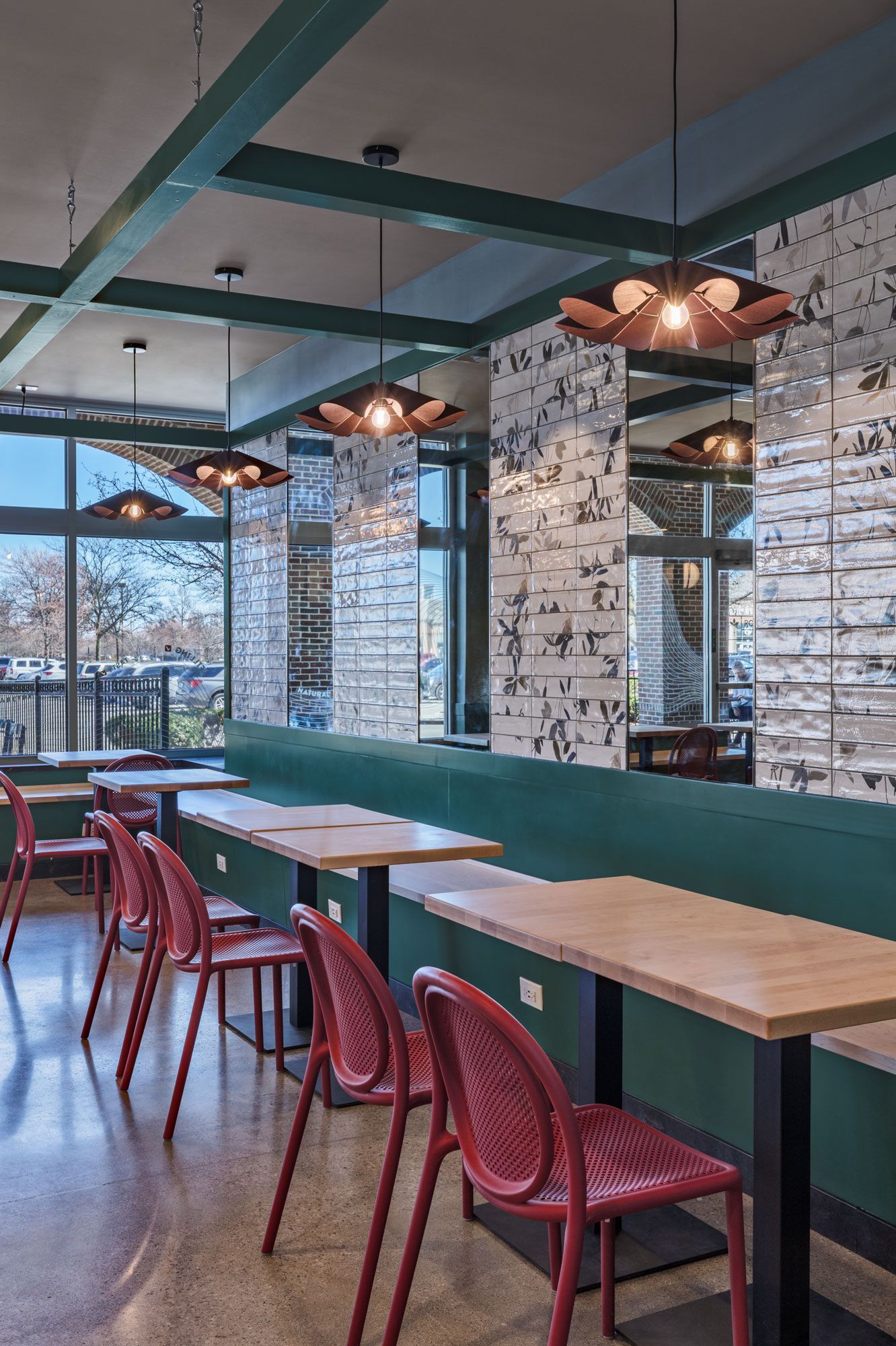 Roots Natural Kitchen's interior with red chairs, wooden tables, and hanging lights against a patterned wall