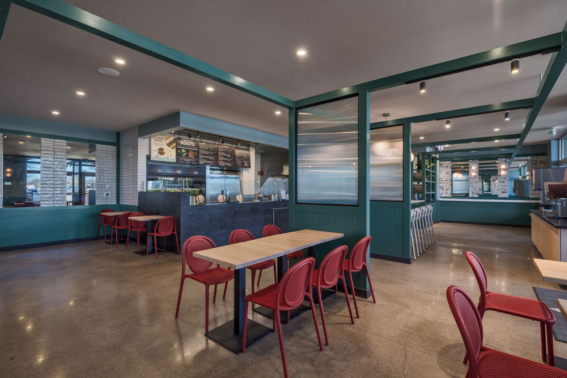 Roots Natural Kitchen with red chairs, blue booths, and concrete floors under pendant lights