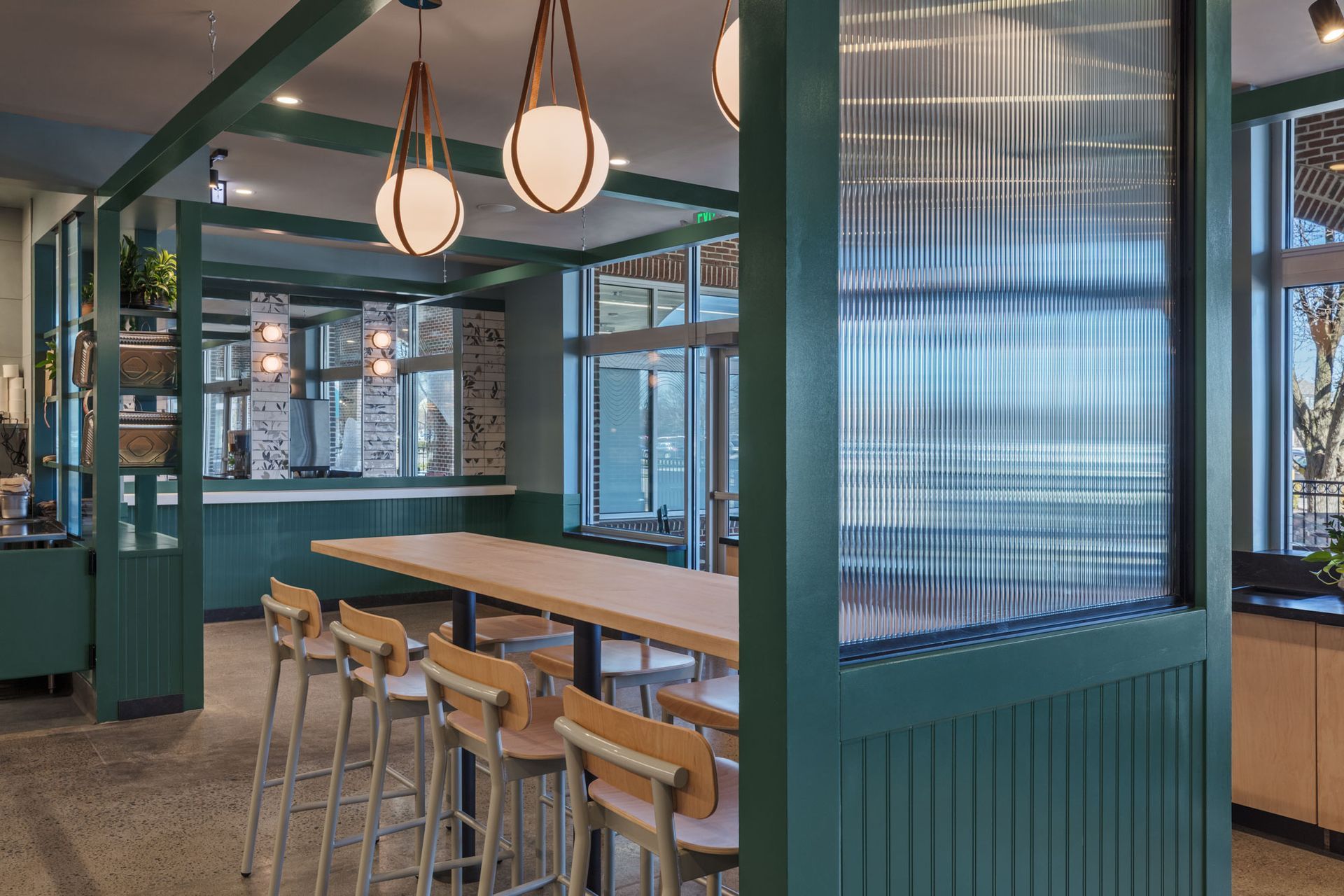 Roots Natural Kitchen's interior with wooden tables, bar stools, teal walls, and hanging pendant lights