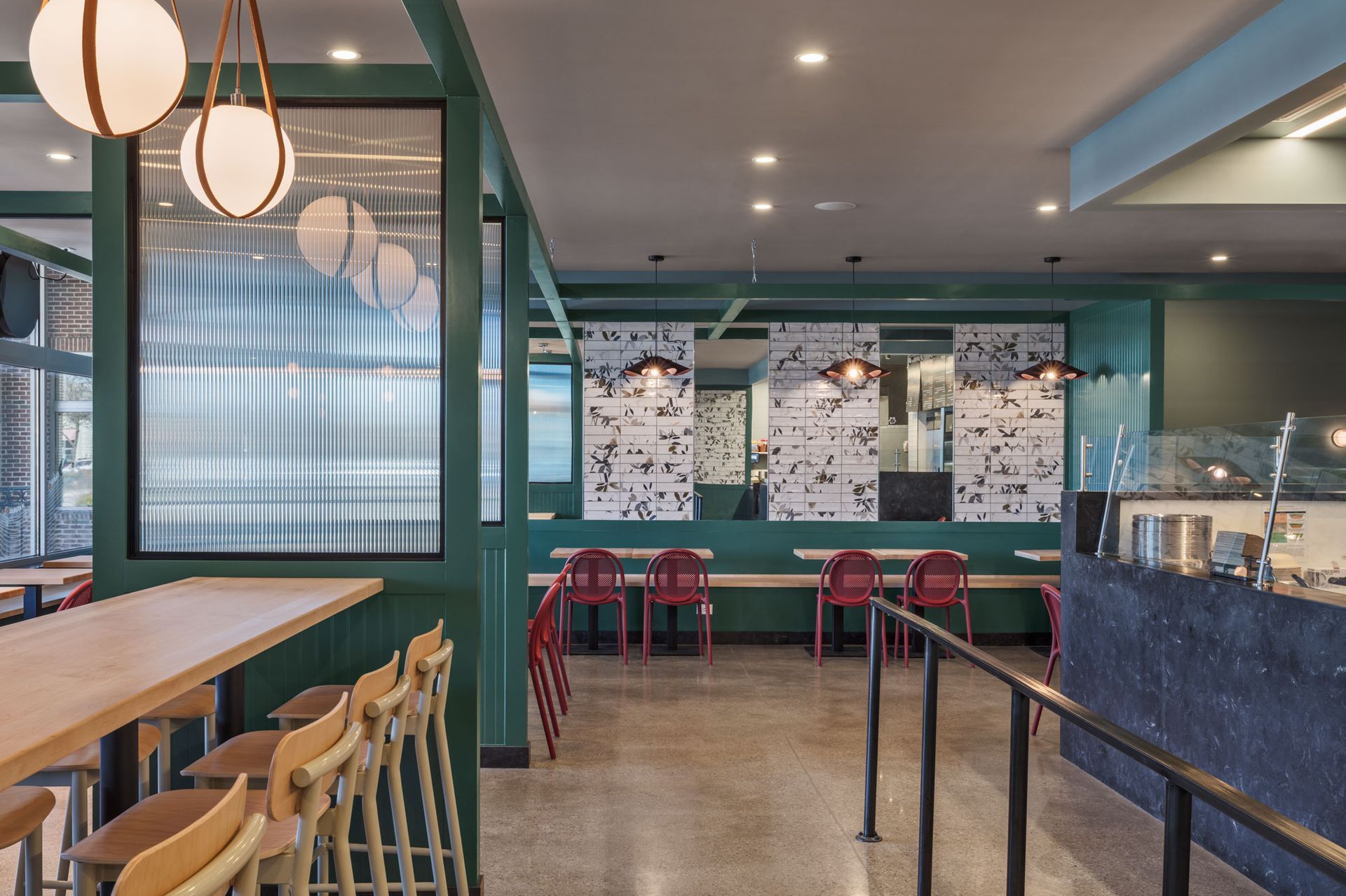Roots Natural Kitchen's interior with teal walls, wooden tables, red chairs, and a glass display counter