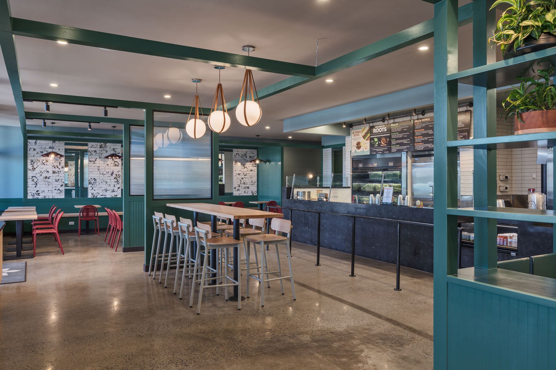 Roots Natural Kitchen's interior with teal walls, bar stools, pendant lights, and an open counter area