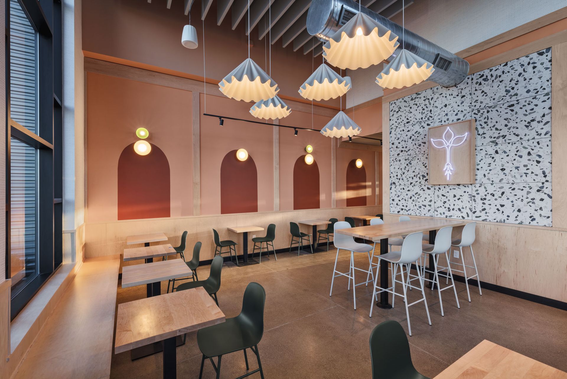 Roots Natural Kitchen's interior with wooden tables, hanging pendant lights, and a mosaic wall and bar stools.