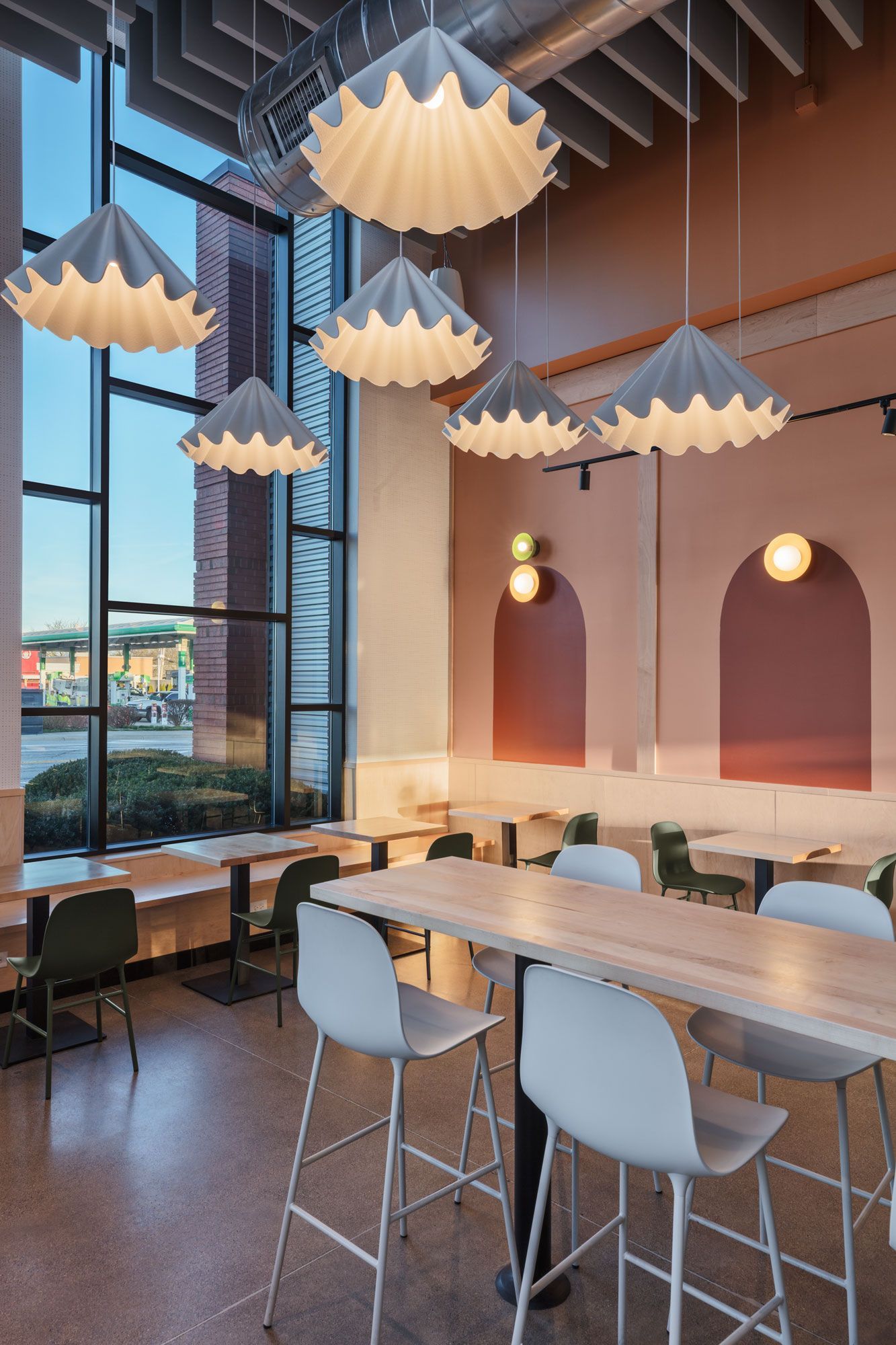 Roots Natural Kitchen's interior with large windows, pendant lights, and wooden tables with white chairs