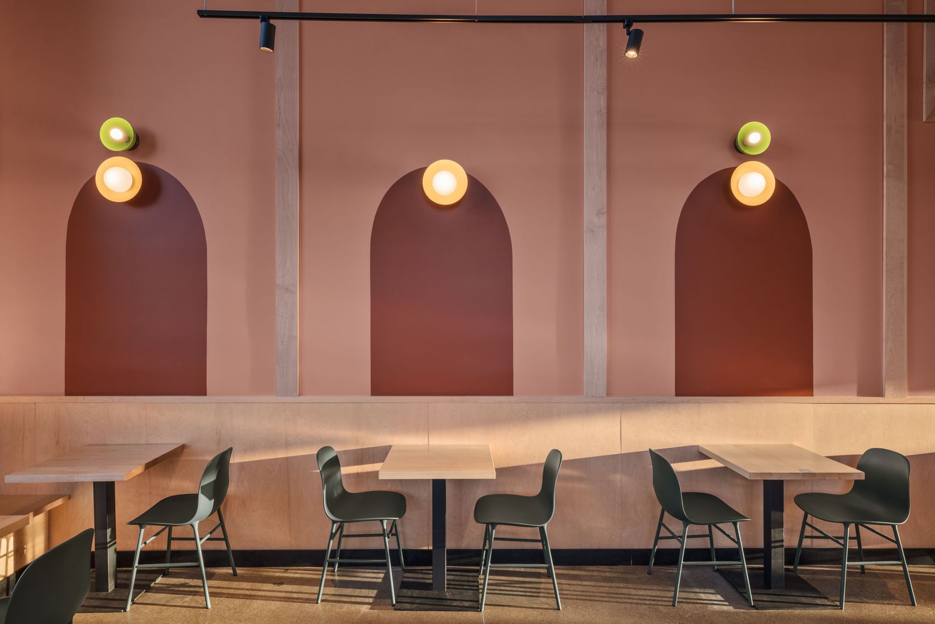 Roots Natural Kitchen's interior with arched wall niches, round lights, and empty chairs and tables by a window.