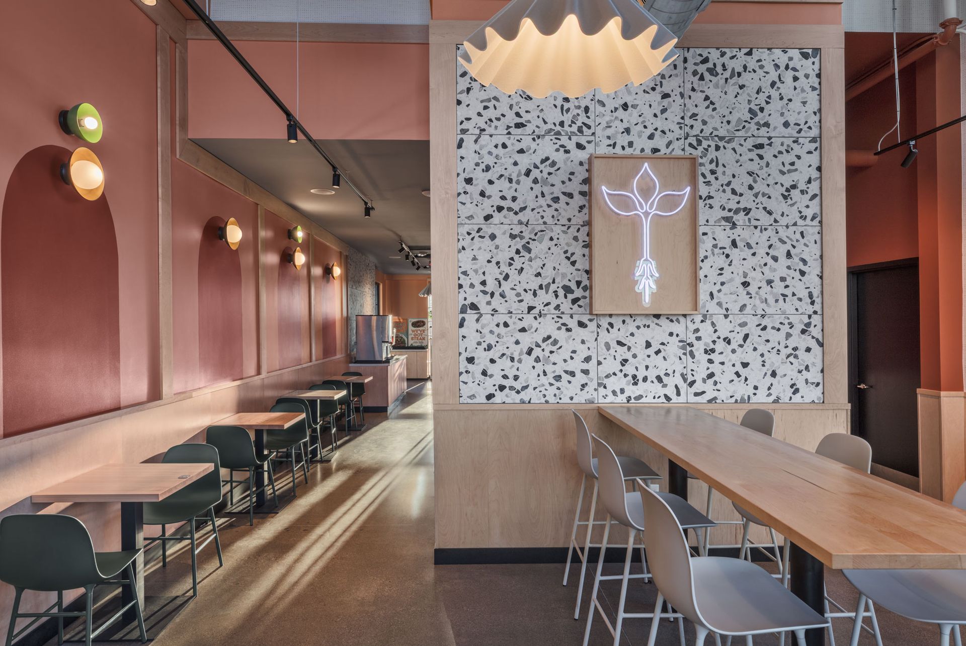 Roots Natural Kitchen's interior with long wooden tables, chairs, pendant lights, and a speckled wall mural