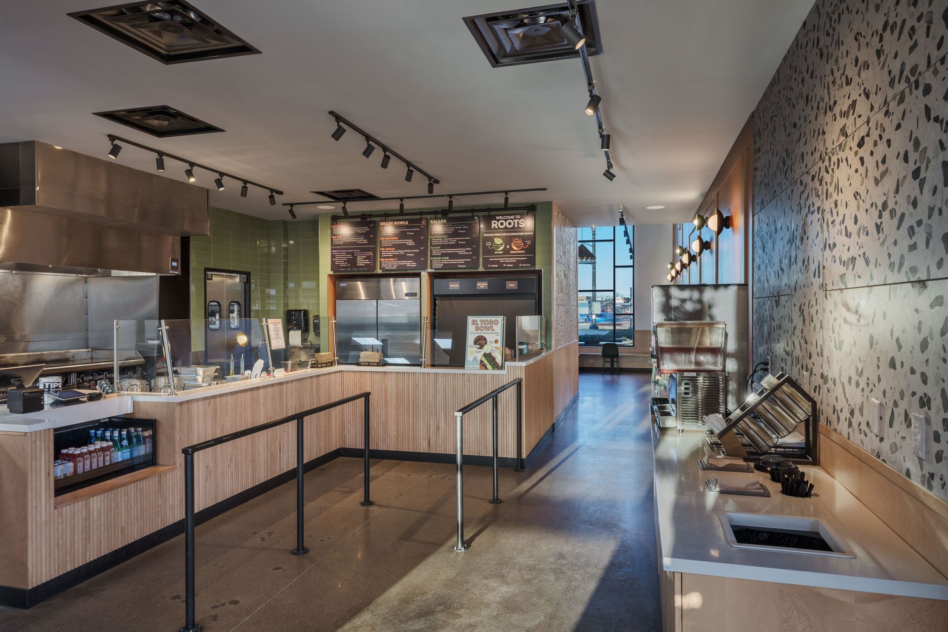 Roots Natural Kitchen's interior with a counter, seating, and track lighting along a patterned wall.