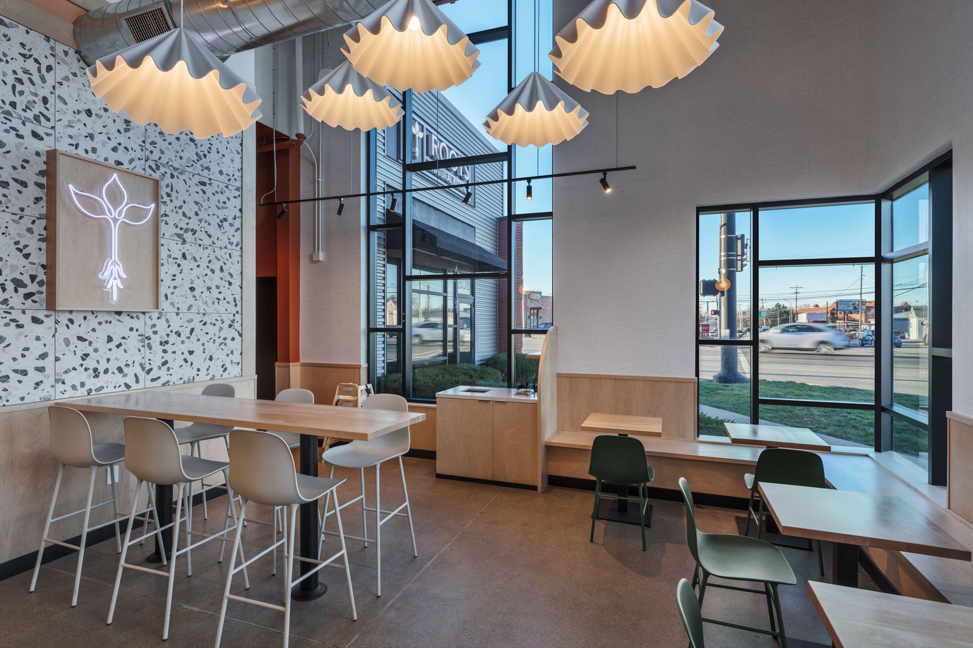 Roots Natural Kitchen's interior with wooden tables, pendant lights, and large windows overlooking a waterfront view