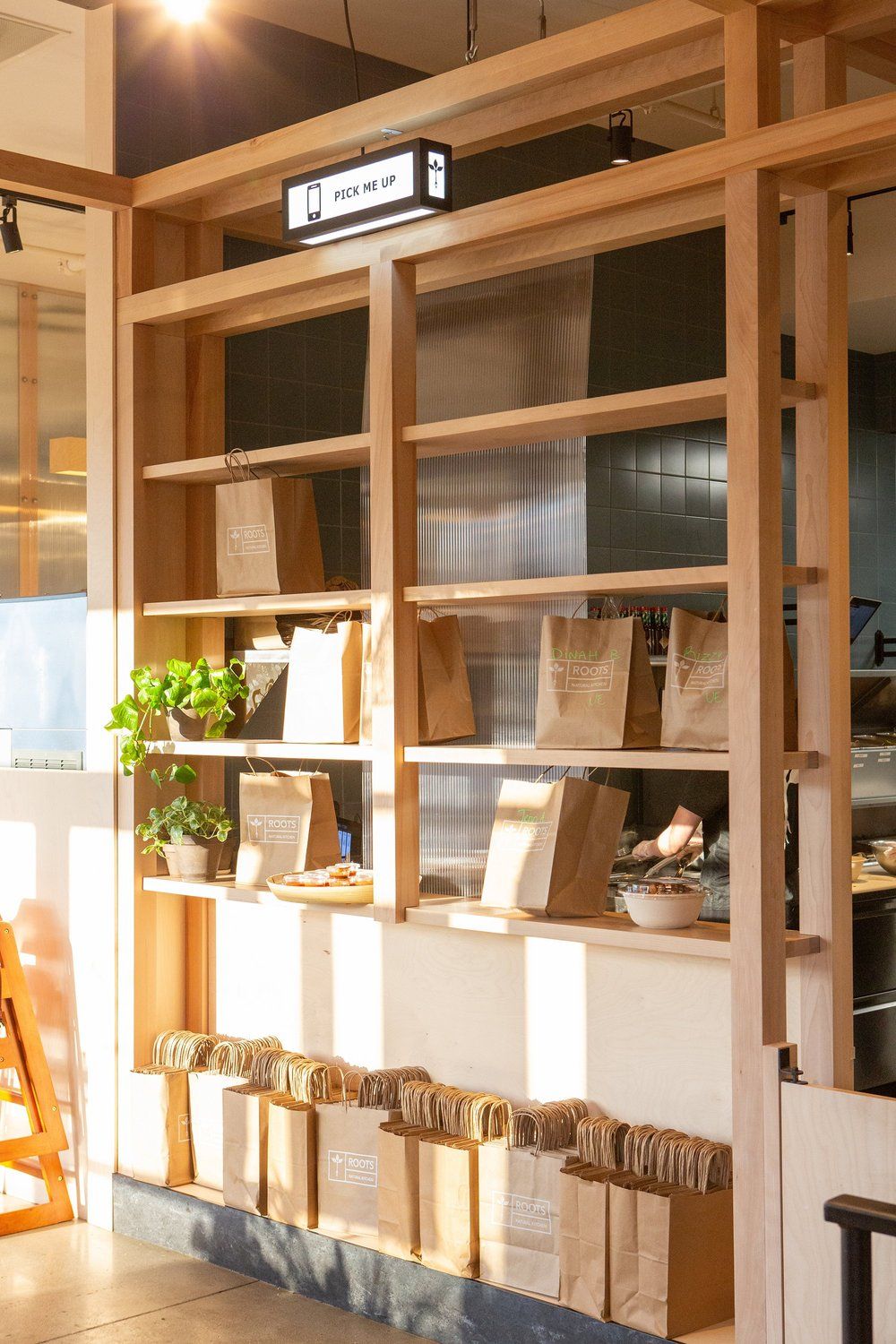 Roots Natural Kitchen display shelves with potted plants, cups, and decor in warm sunlight