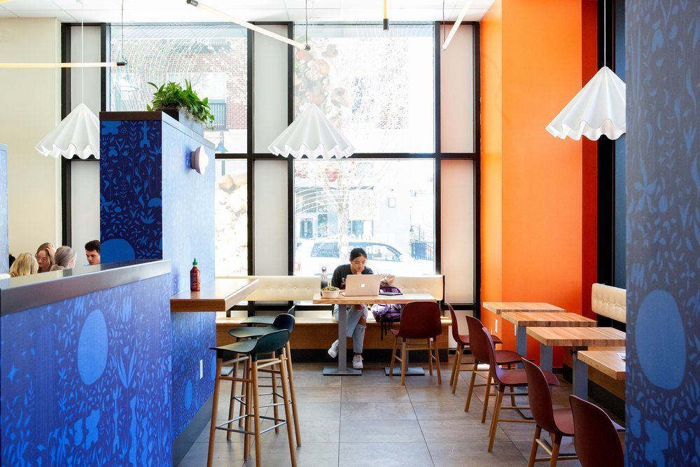 Roots Natural Kitchen's interior with blue and orange walls, hanging lamps, and a few people seated at tables