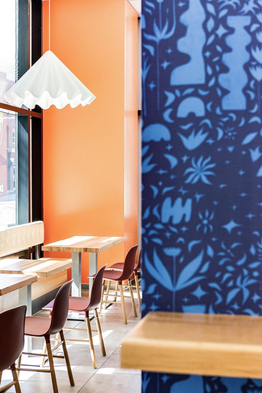 Roots Natural Kitchen's interior with orange walls, blue patterned panel, and empty wooden tables and chairs