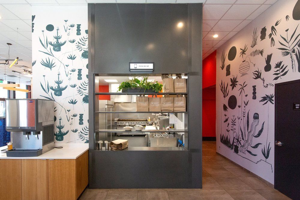 Roots Natural Kitchen's hallway with a central display cabinet, wood counter, and botanical wall murals
