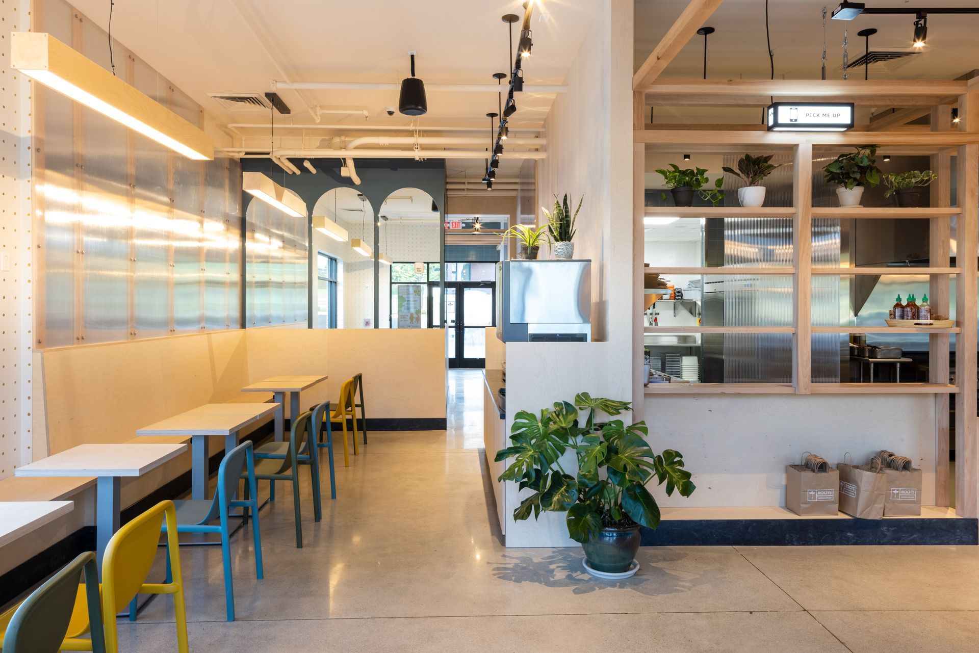 Roots Natural Kitchen with long tables, yellow chairs, plants, and glass partitions