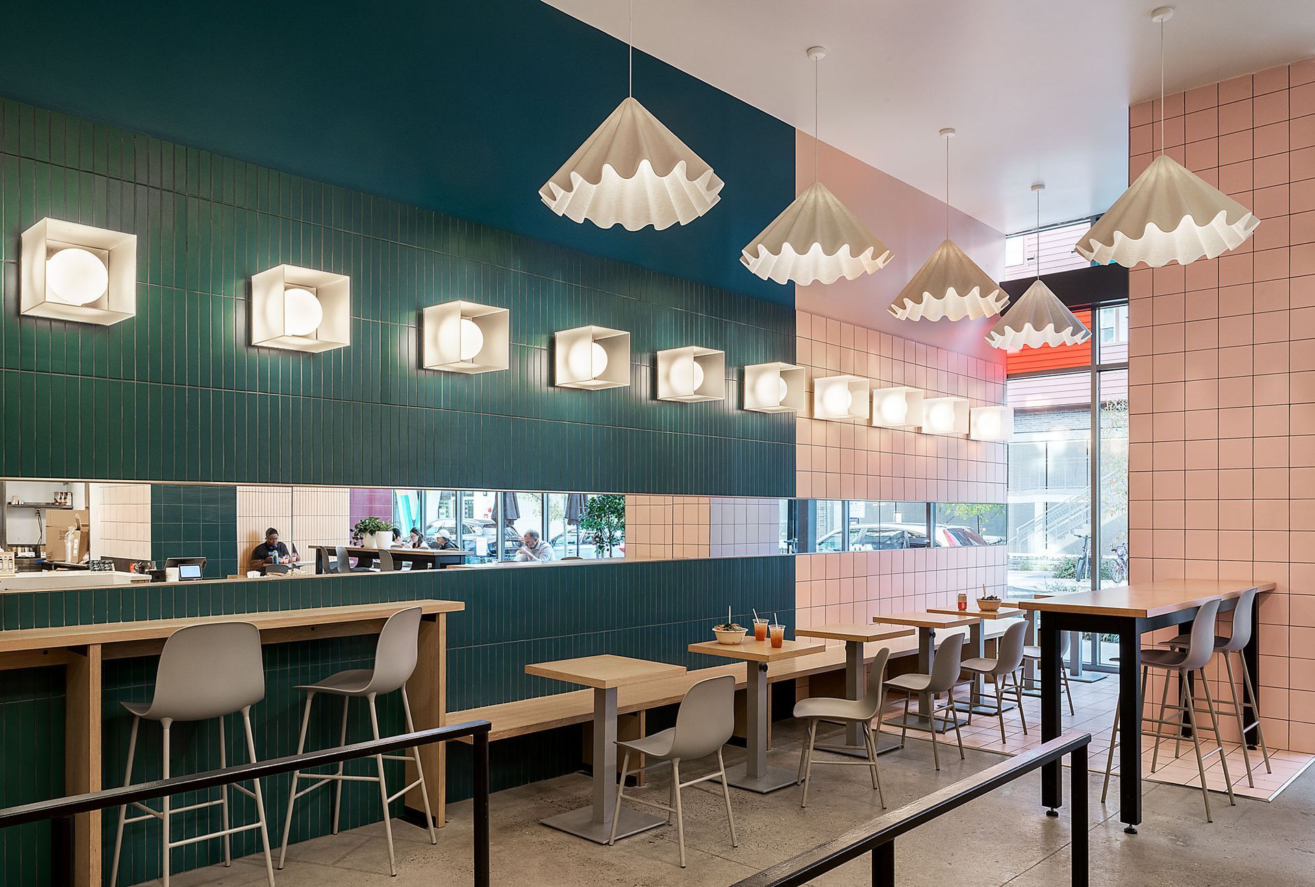 Restaurant interior with teal and pink walls, pendant lights, and tables with chairs.