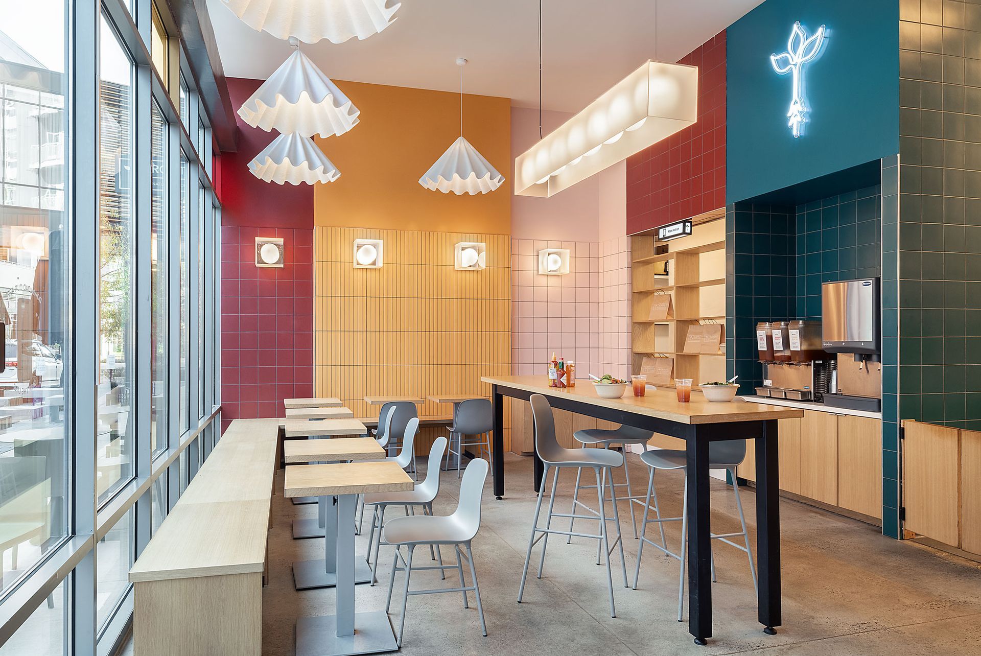 Roots Natural Kitchen bright, modern interior with colorful paneled walls, wooden tables, metal chairs, and hanging pendant lights.