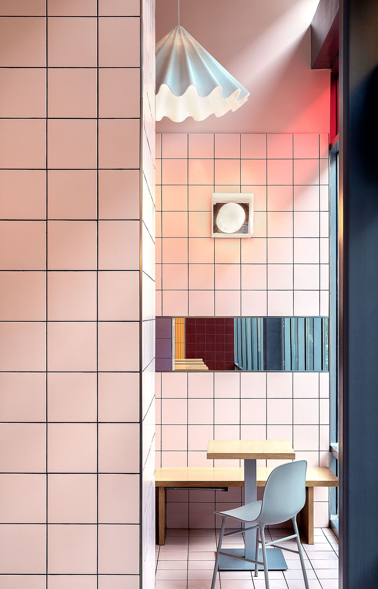 Pink-tiled cafe interior with a table and chair, natural light, and a decorative pendant lamp.