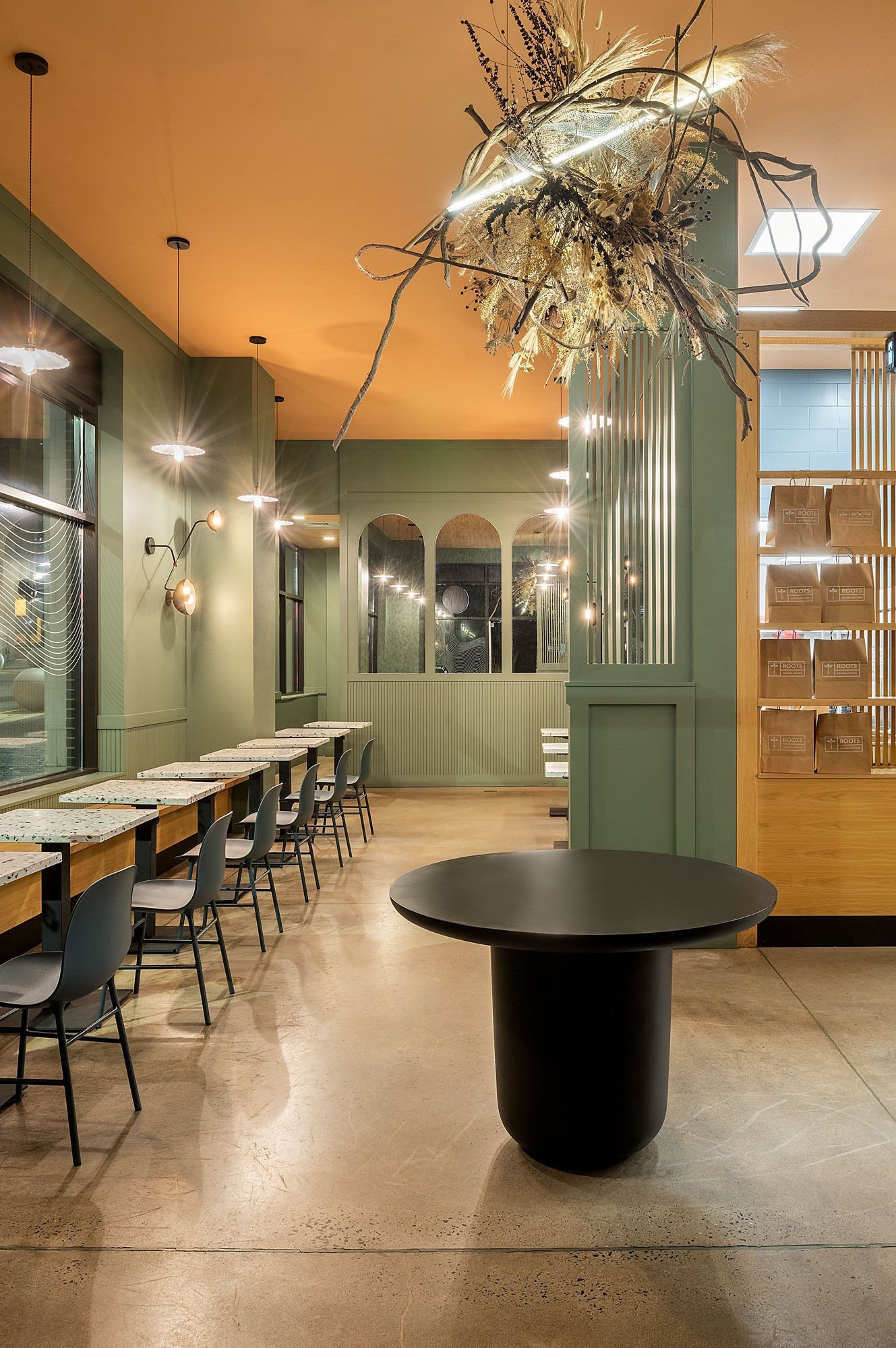 Roots Natural Kitchen's interior with long communal table, chairs, pendant lights, and a round black table in front