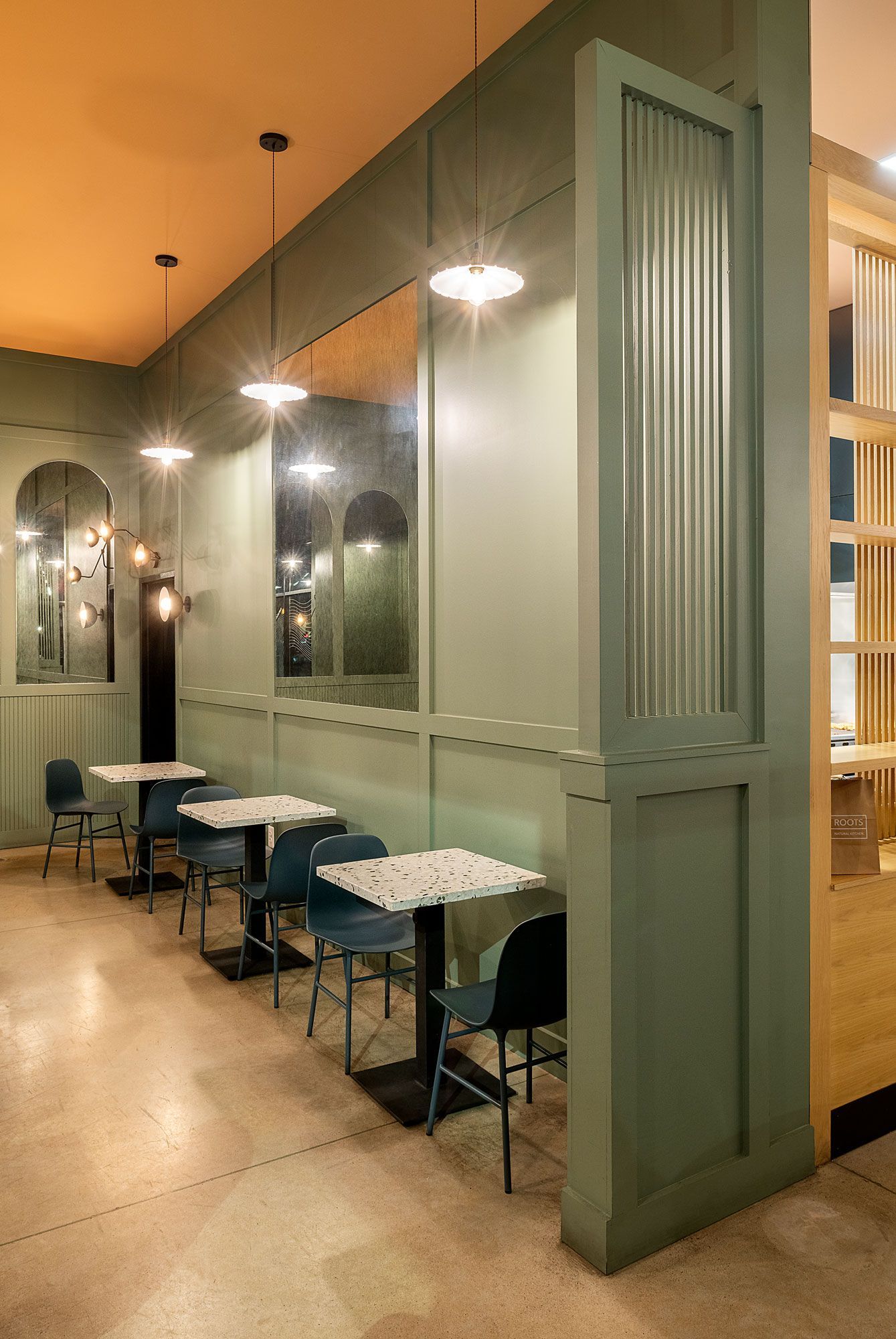 Roots Natural Kitchen's booth seating with green-paneled walls, mirrors, and small tables along a softly lit corridor