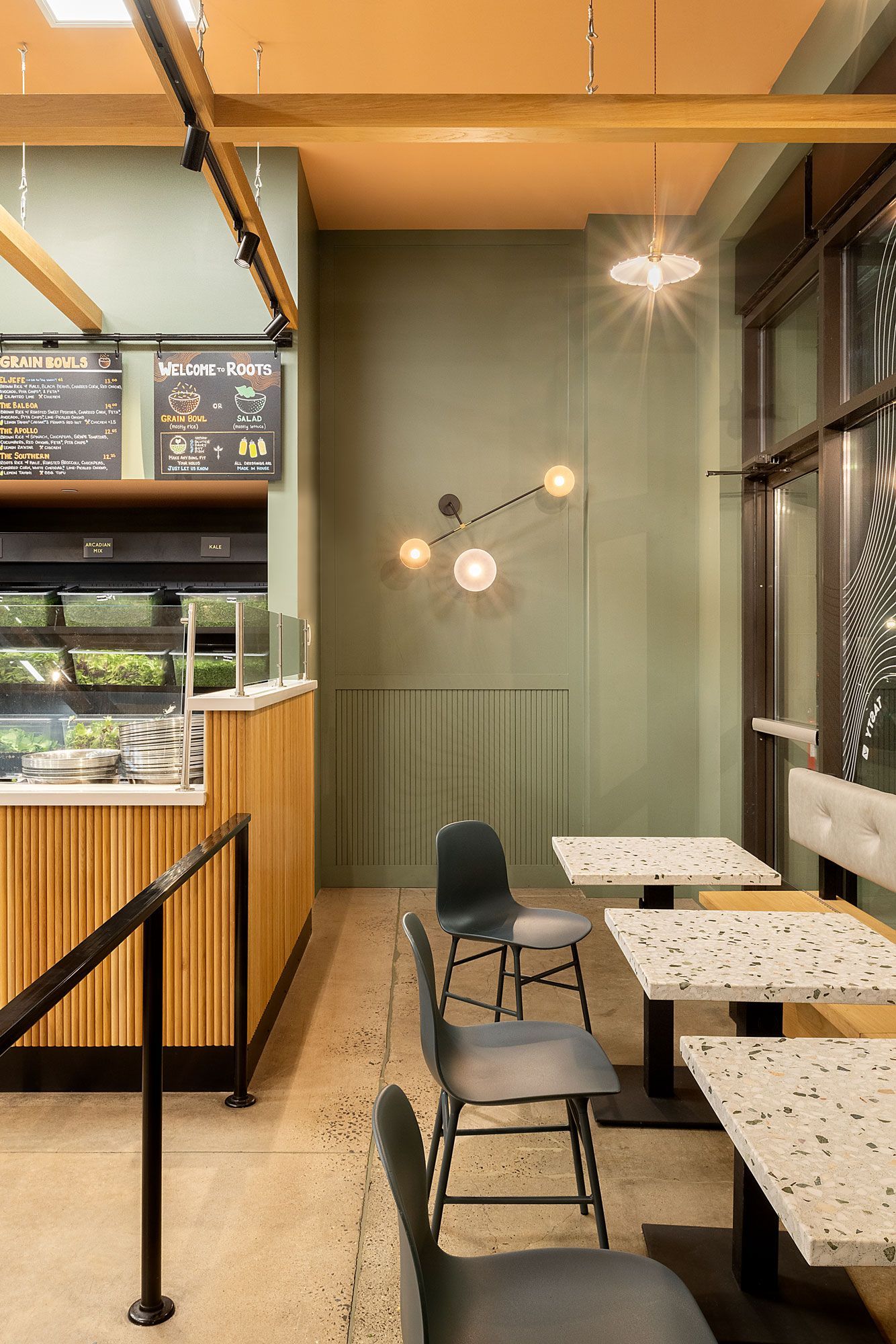 Roots Natural Kitchen's seating area with wood counter, marble tables, black chairs, and warm pendant lights