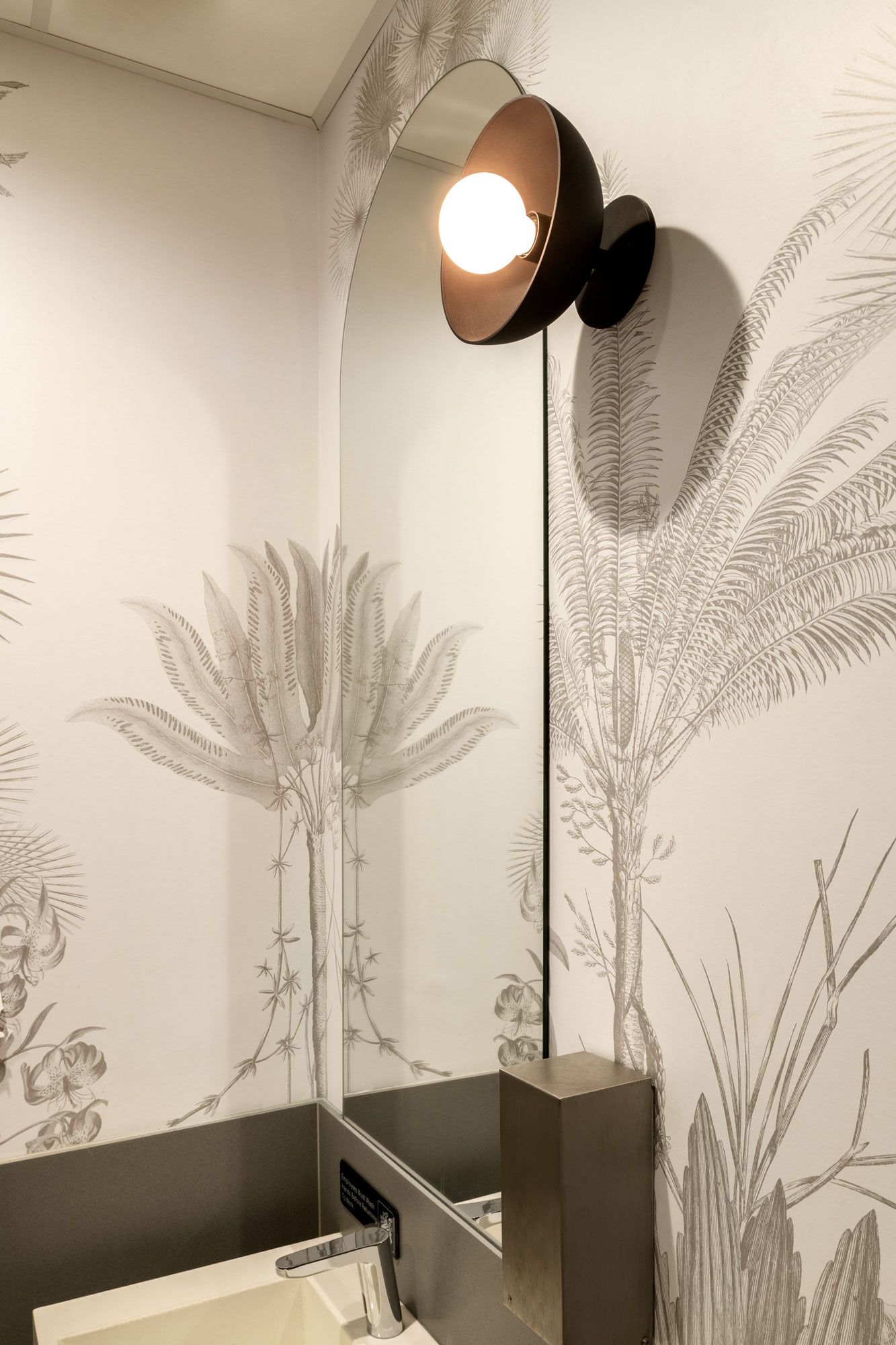 Roots Natural Kitchen's corner wall sconce lamp above a small table, casting warm light on botanical wall art.