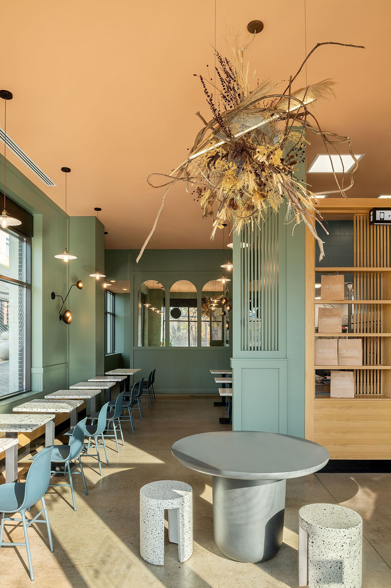 Roots Natural Kitchen's interior with teal walls, long counter seating, round table, and hanging dried floral centerpiece