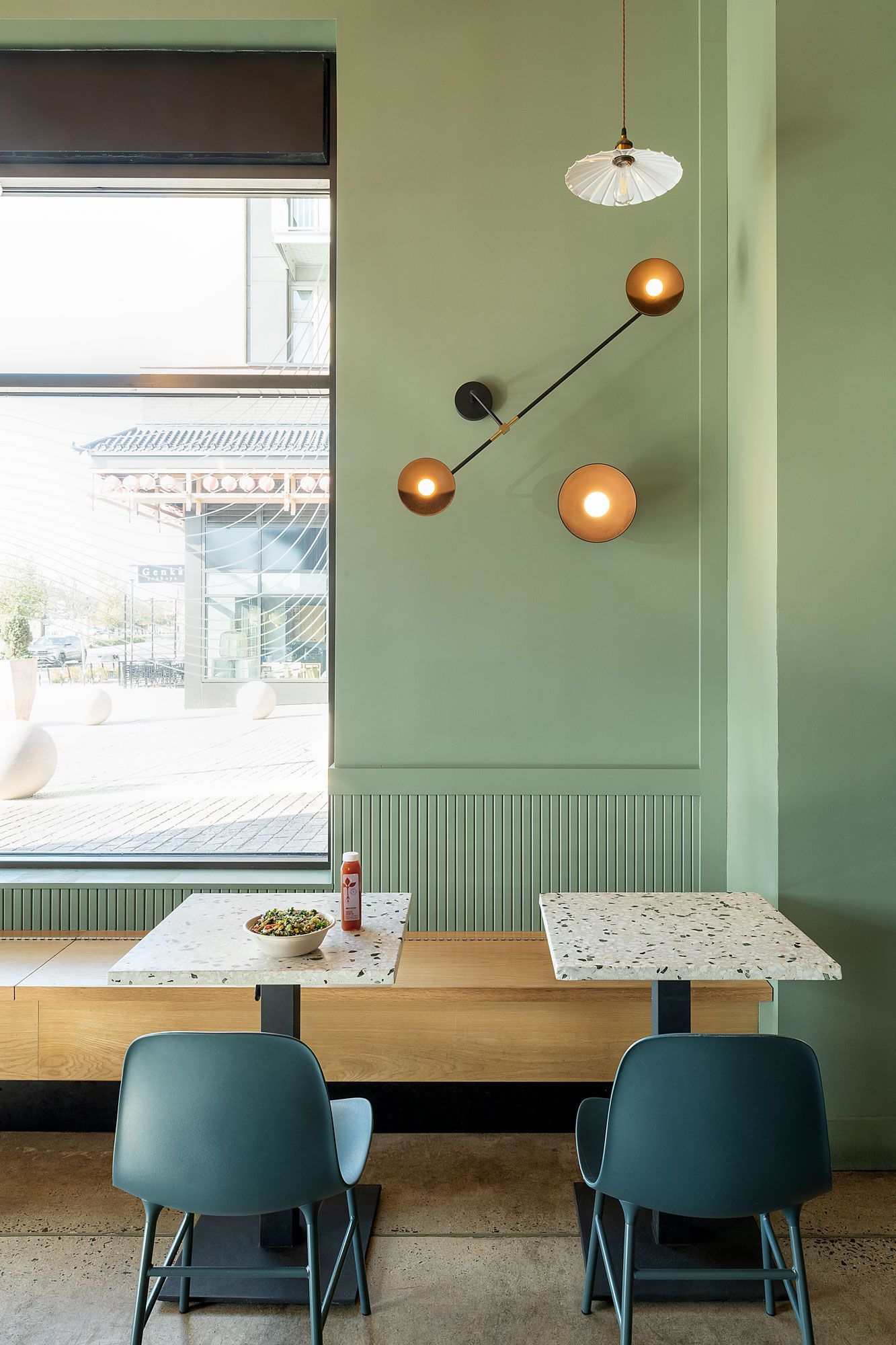 Roots Natural Kitchen's interior with mint walls, pendant lights, wooden bench seating, and blue chairs by a window
