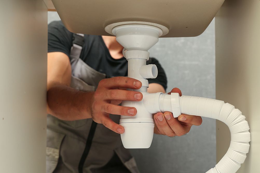 A man is fixing a sink pipe under a sink.