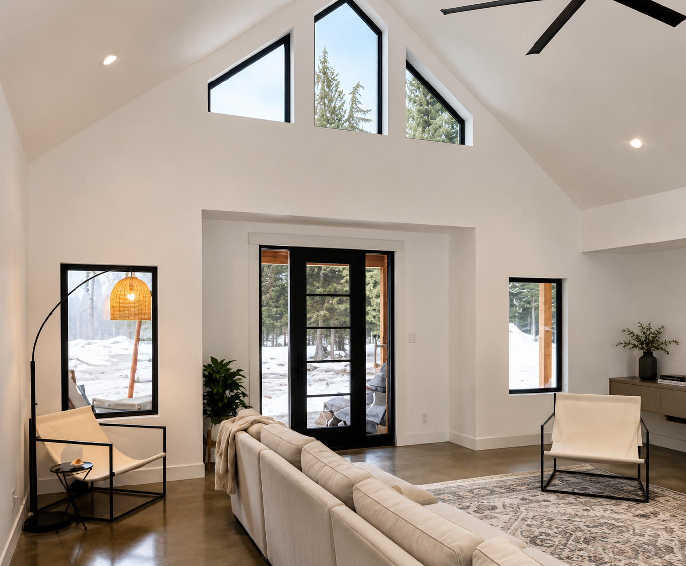 Bright modern living room with vaulted ceiling, black-trimmed windows, beige sofa, and lamp chairs