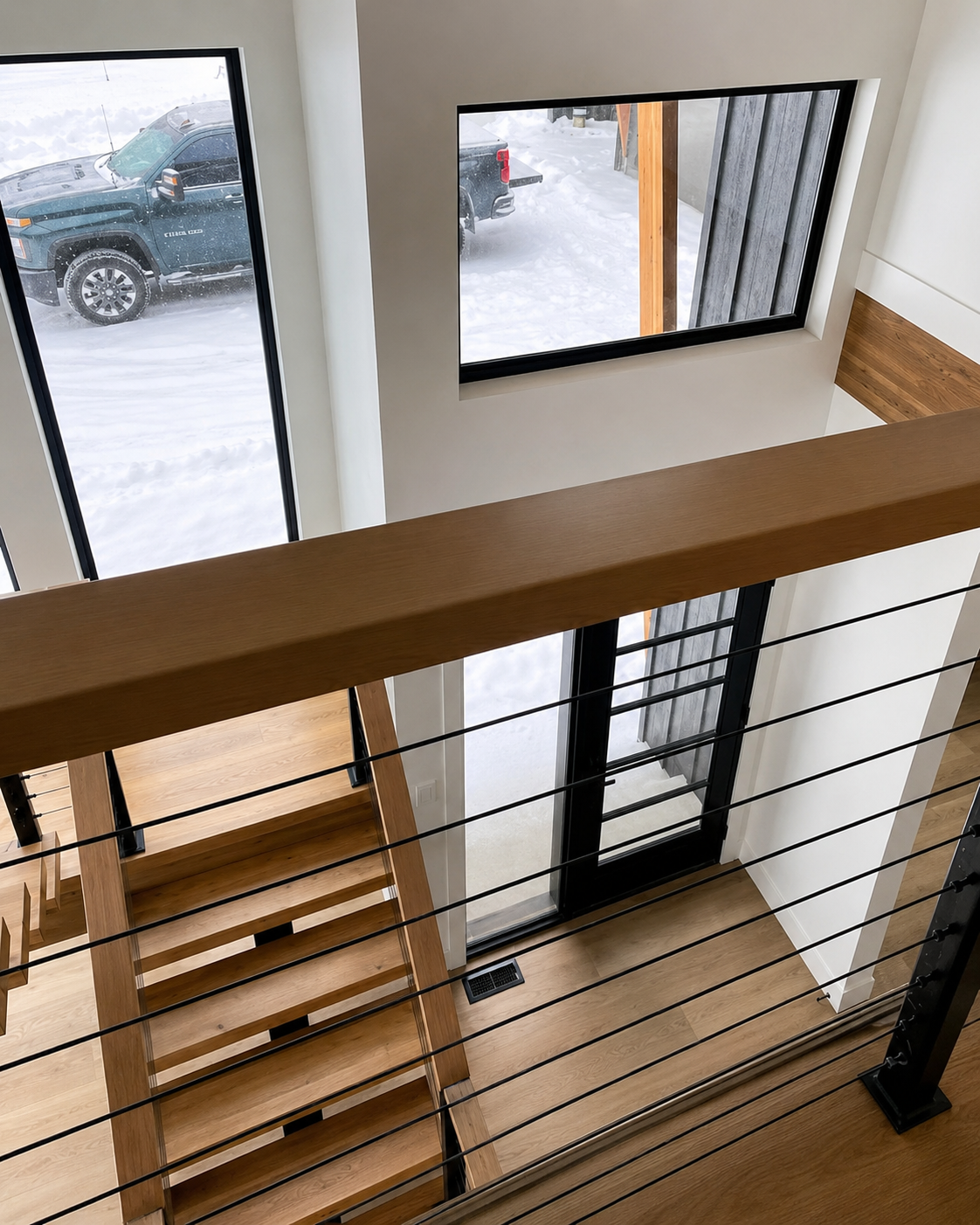 Stairwell with wood steps, black railing, and large windows looking onto a snowy parking lot