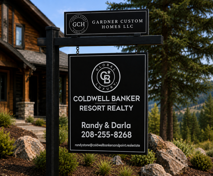 Coldwell Banker Resort Realty sign beside a house, with green trees and mountains in the background.