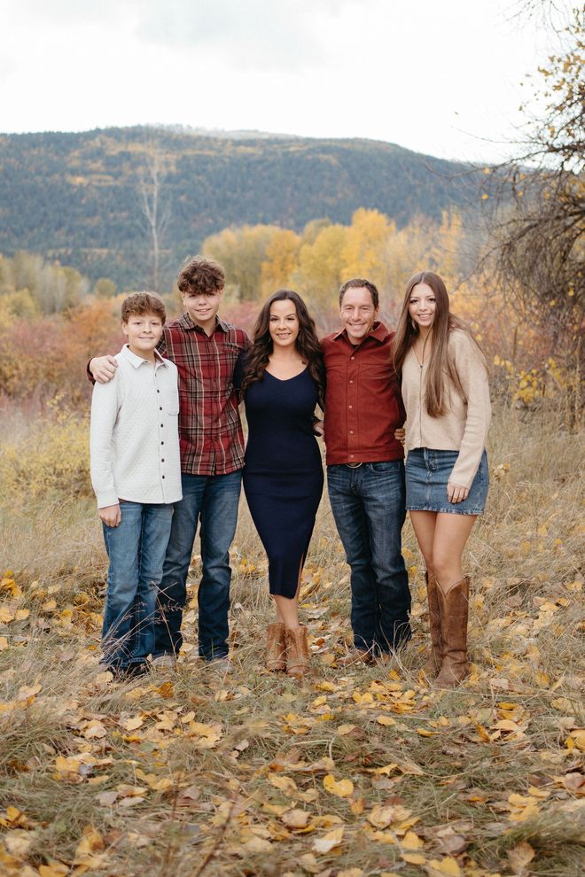 Five people standing together on a leaf-covered path with mountains and autumn trees in the background