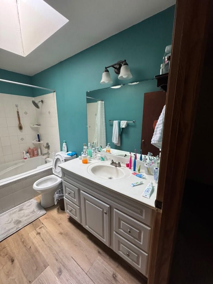 Bathroom with teal walls, white vanity, mirror, toilet, and bathtub with shower curtain.